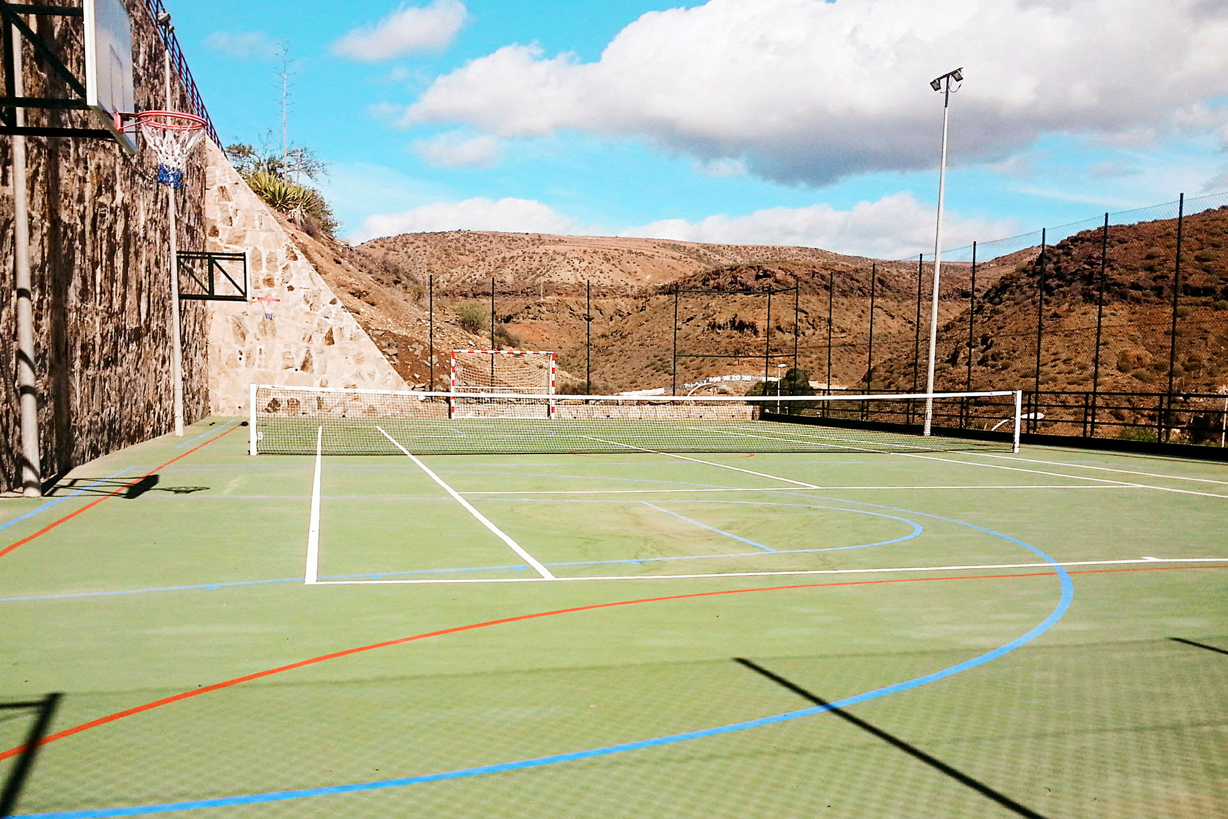 Bild på en utomhus idrottsplats med nät för tennis, fotbollsmål och basketkorg. (AI-genererad text)