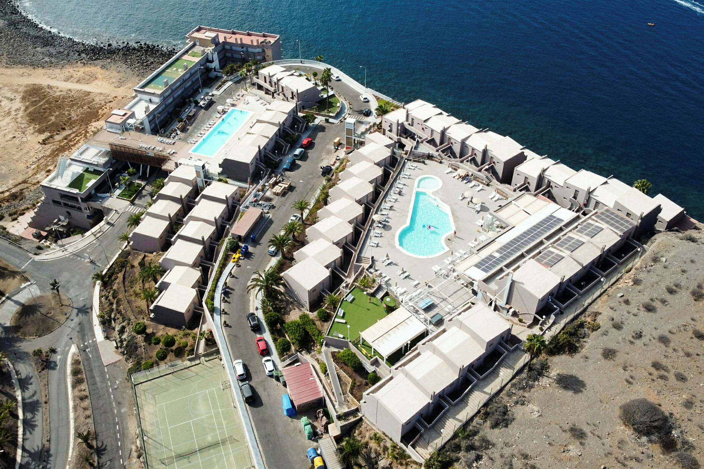 Flygfoto av ett stort semesterkomplex vid havet med pooler och byggnader. (AI-genererad text)