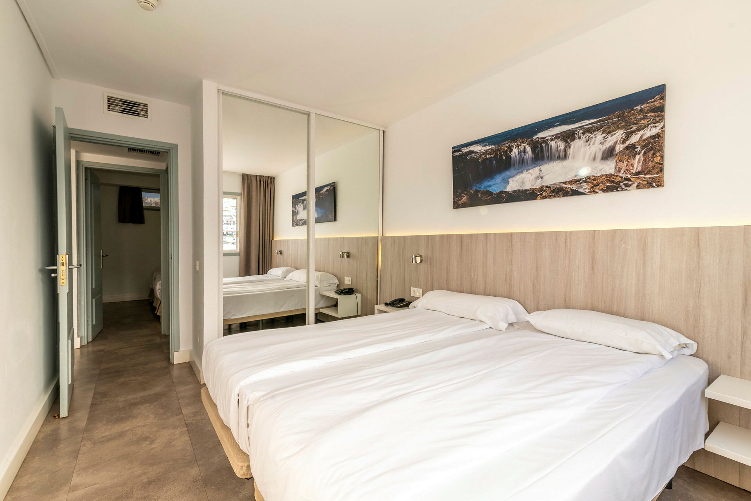 Ett hotellrum med två enkelsängar, en spegelvägg och dekorationer. (AI-genererad text)