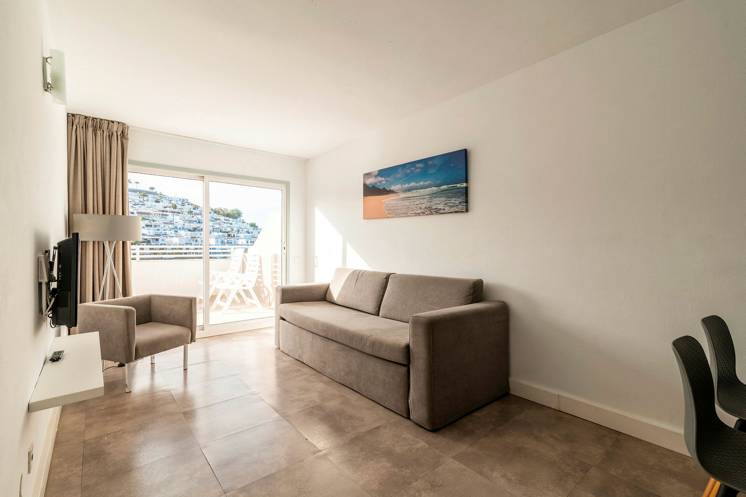 Ett hotellrum med en beige soffa och en fåtölj samt en balkong med utsikt. (AI-genererad text)