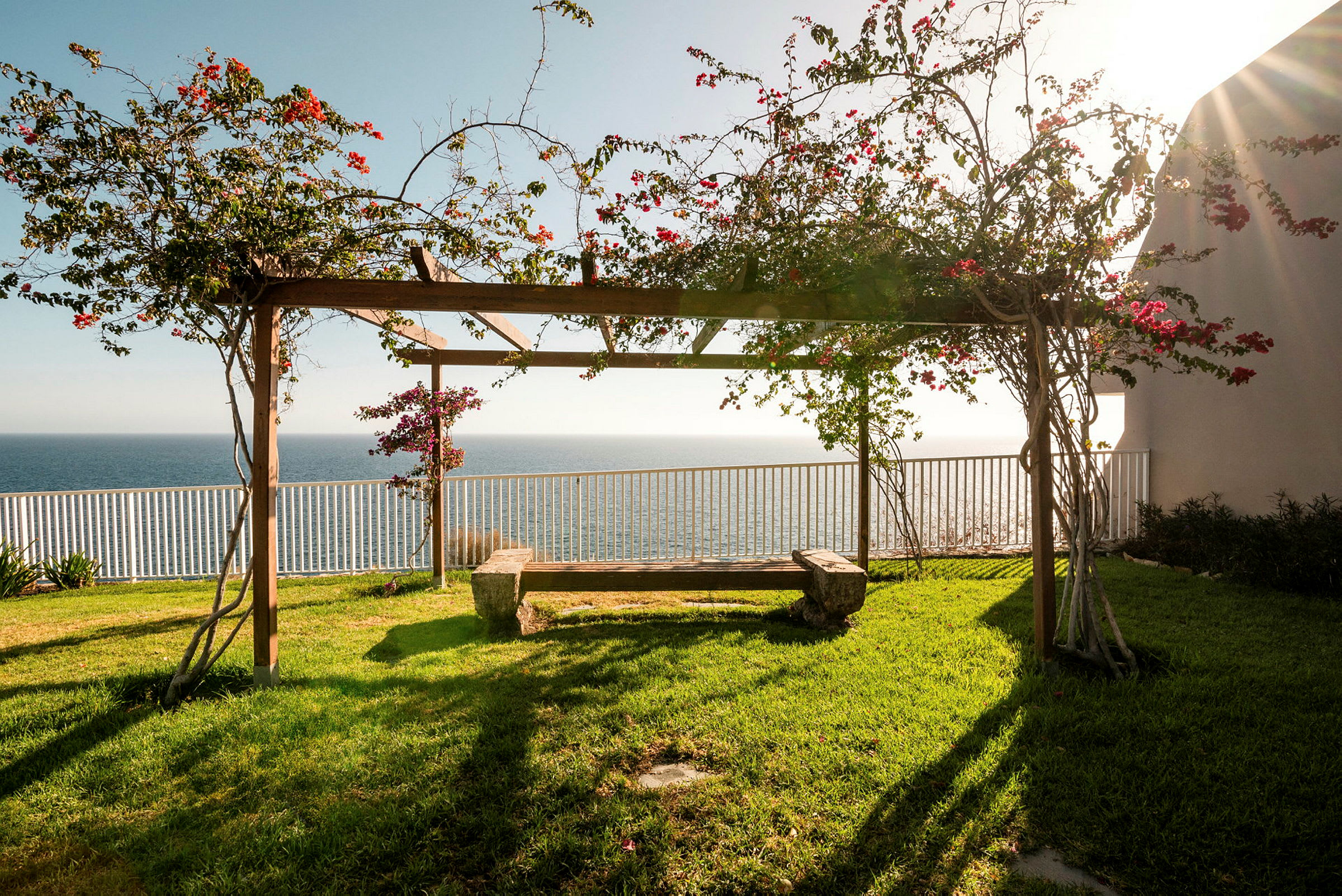 En pergola med blommande växter och bänk, havet i bakgrunden. (AI-genererad text)