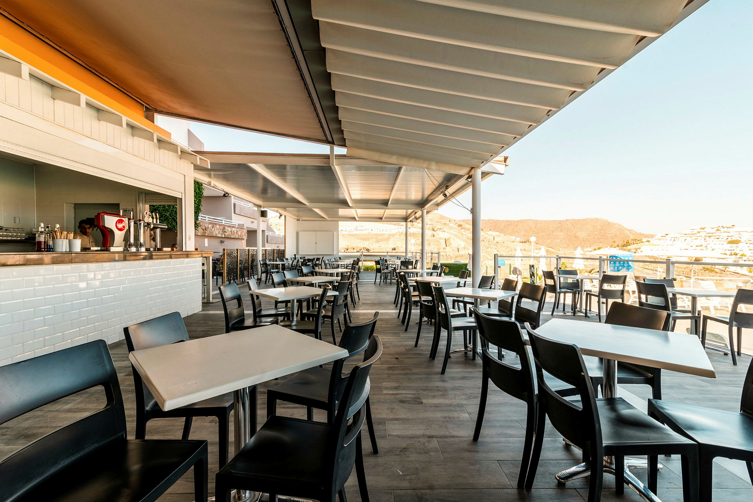 Utomhusrestaurang med moderna bord och stolar under en täckt pergola. (AI-genererad text)