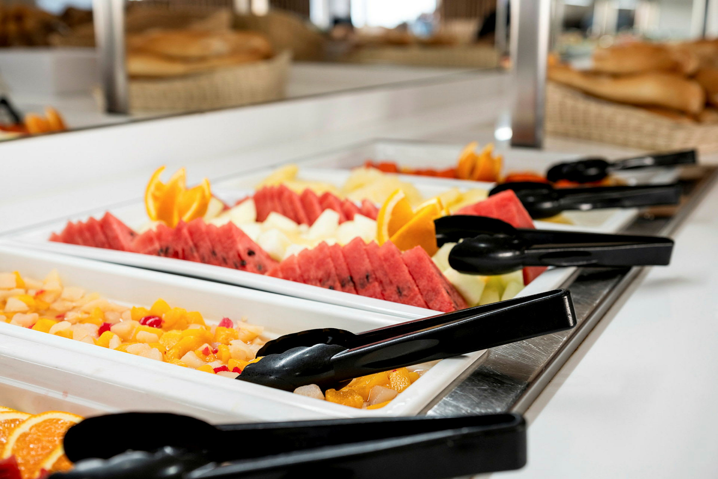 Buffébord med färsk frukt och sallad, inklusive meloner, apelsinskivor och tänger. (AI-genererad text)