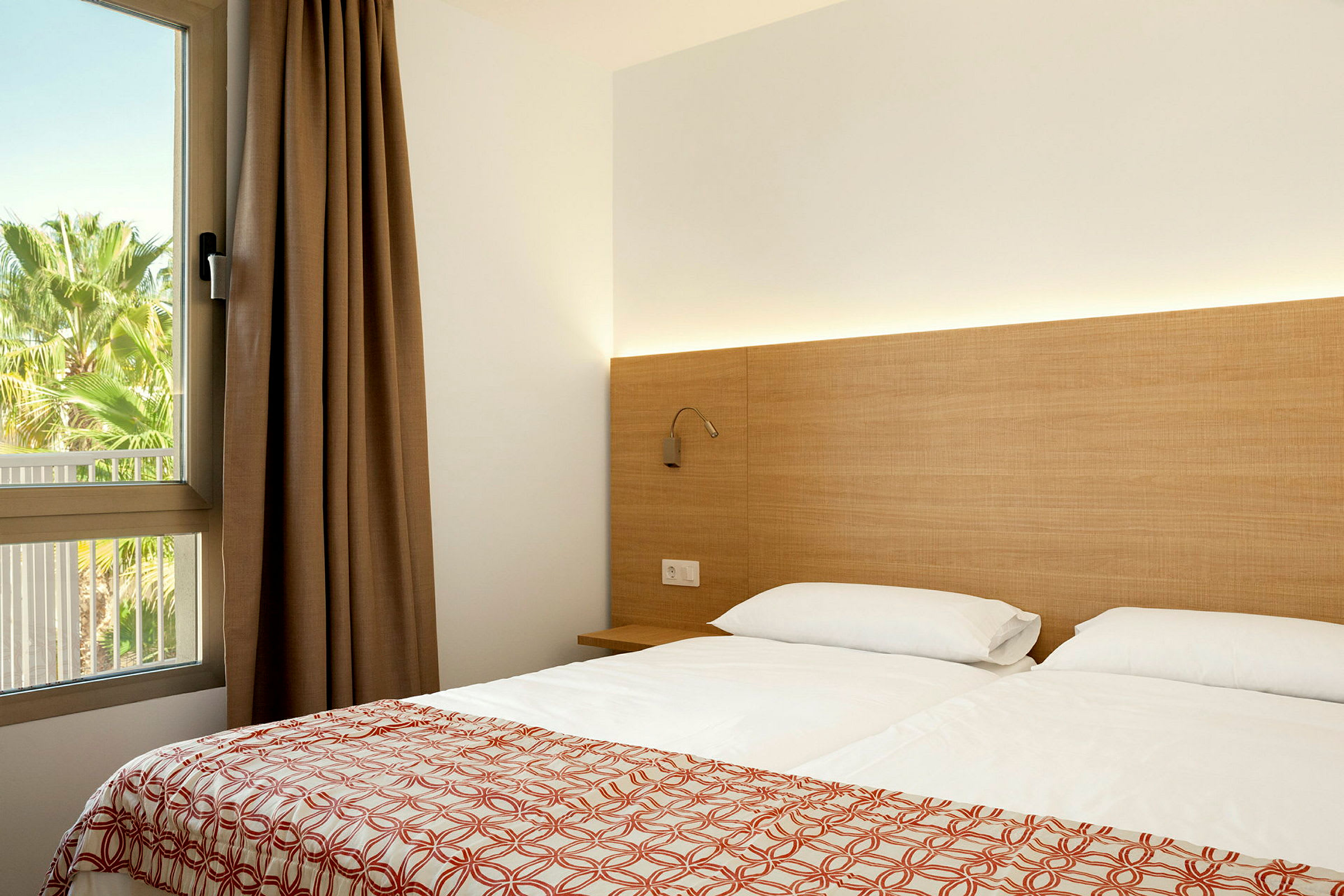 Modernt hotellrum med en dubbelsäng, sängbord och en fönsterutsikt mot grönska. (AI-genererad text)