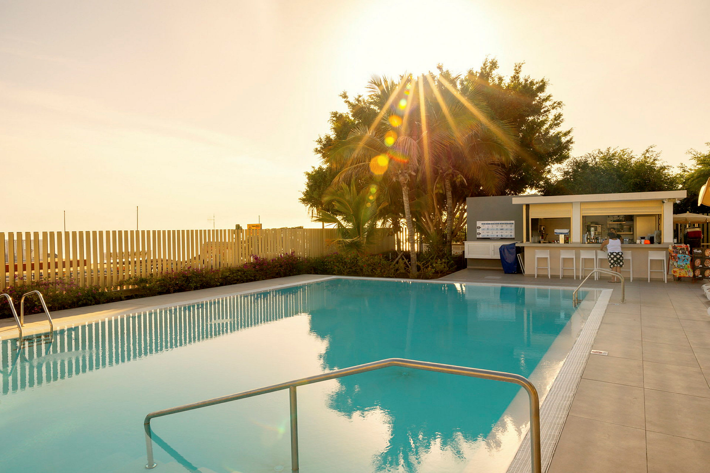 En swimmingpool vid solnedgången med ett litet kafé vid sidan. (AI-genererad text)