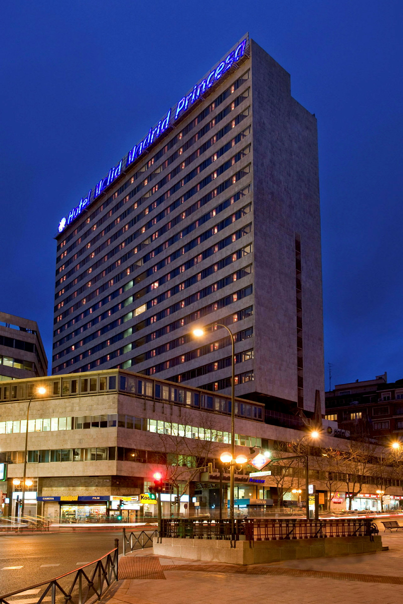 Ett hotell under kvällstid med upplysta fönster och en blå skylt på toppen som lyser upp byggnaden. (AI-genererad text)