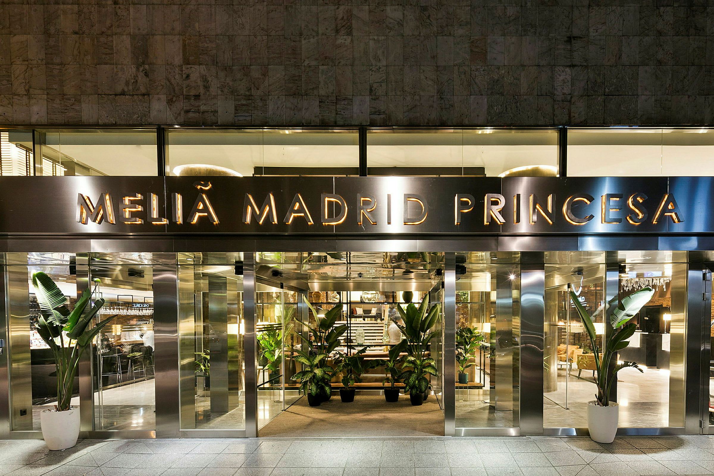 Entrén till hotellet Melia Madrid Princesa, med glasdörrar och dekorativa växter vid ingången. (AI-genererad text)