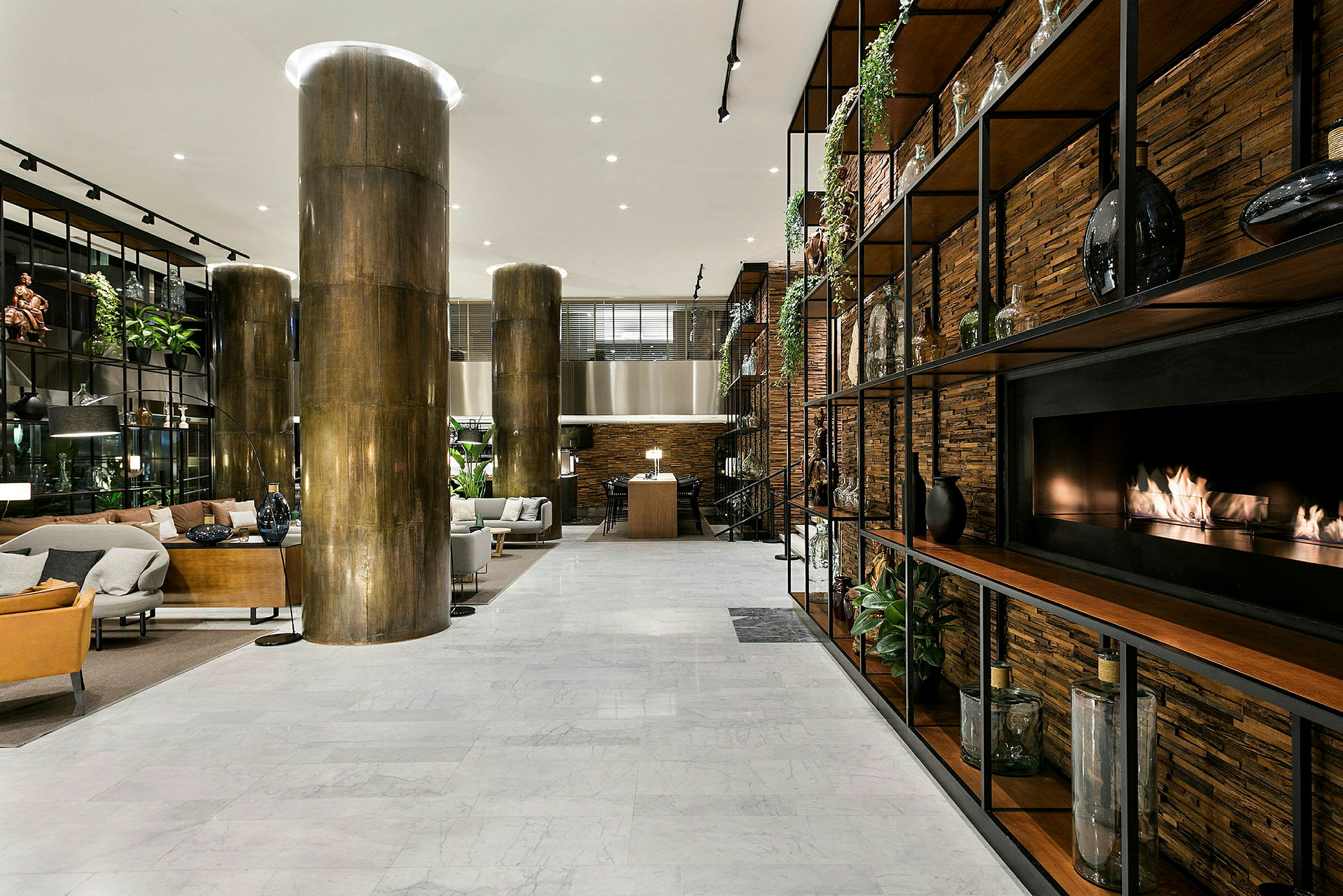 Ett modernt hotellobbyområde med sittgrupper, marmorgolv, stora pelare och en eldstad integrerad i en hyllvägg. (AI-genererad text)