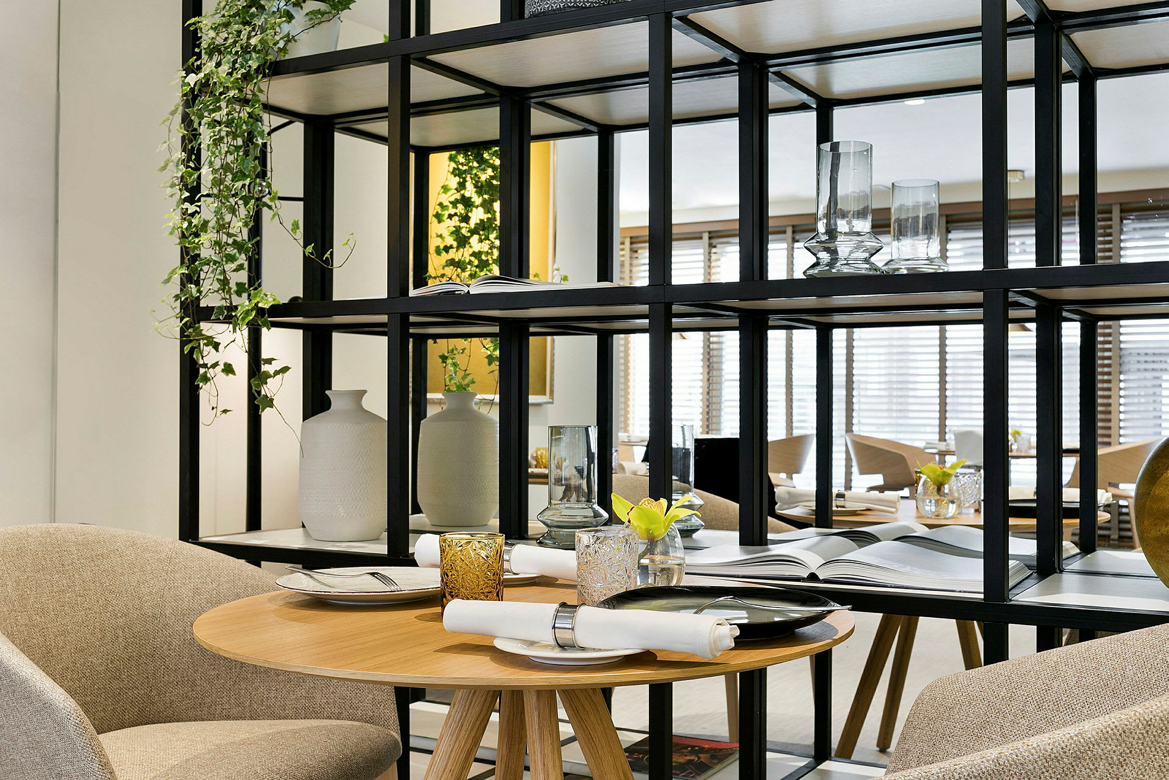 Ett elegant uppdukat bord med servett och glas, omringat av dekorativa hyllor och växter. (AI-genererad text)