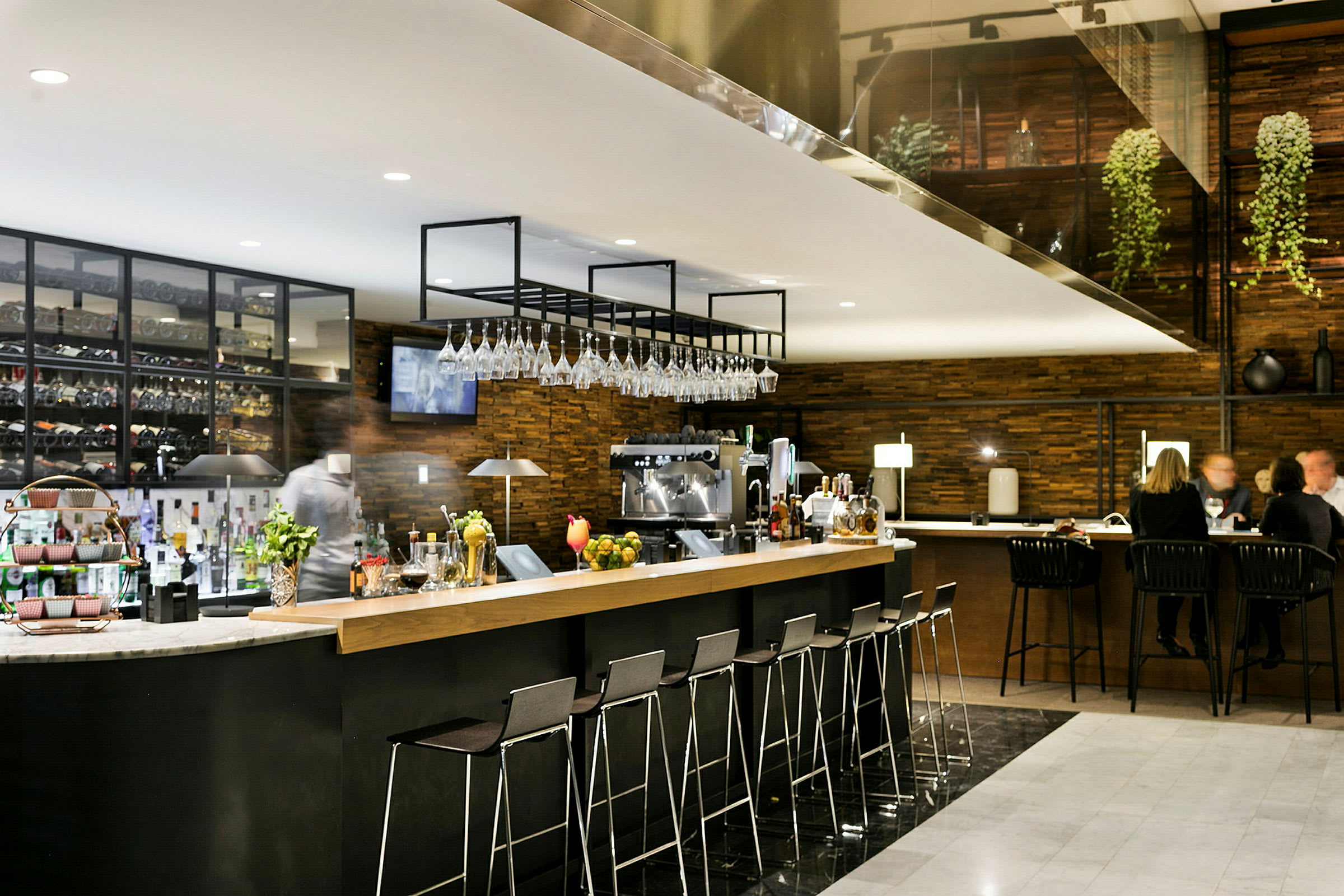 En modern bar med barstolar och upphängda vinglas, flaskor och tillbehör synliga. (AI-genererad text)