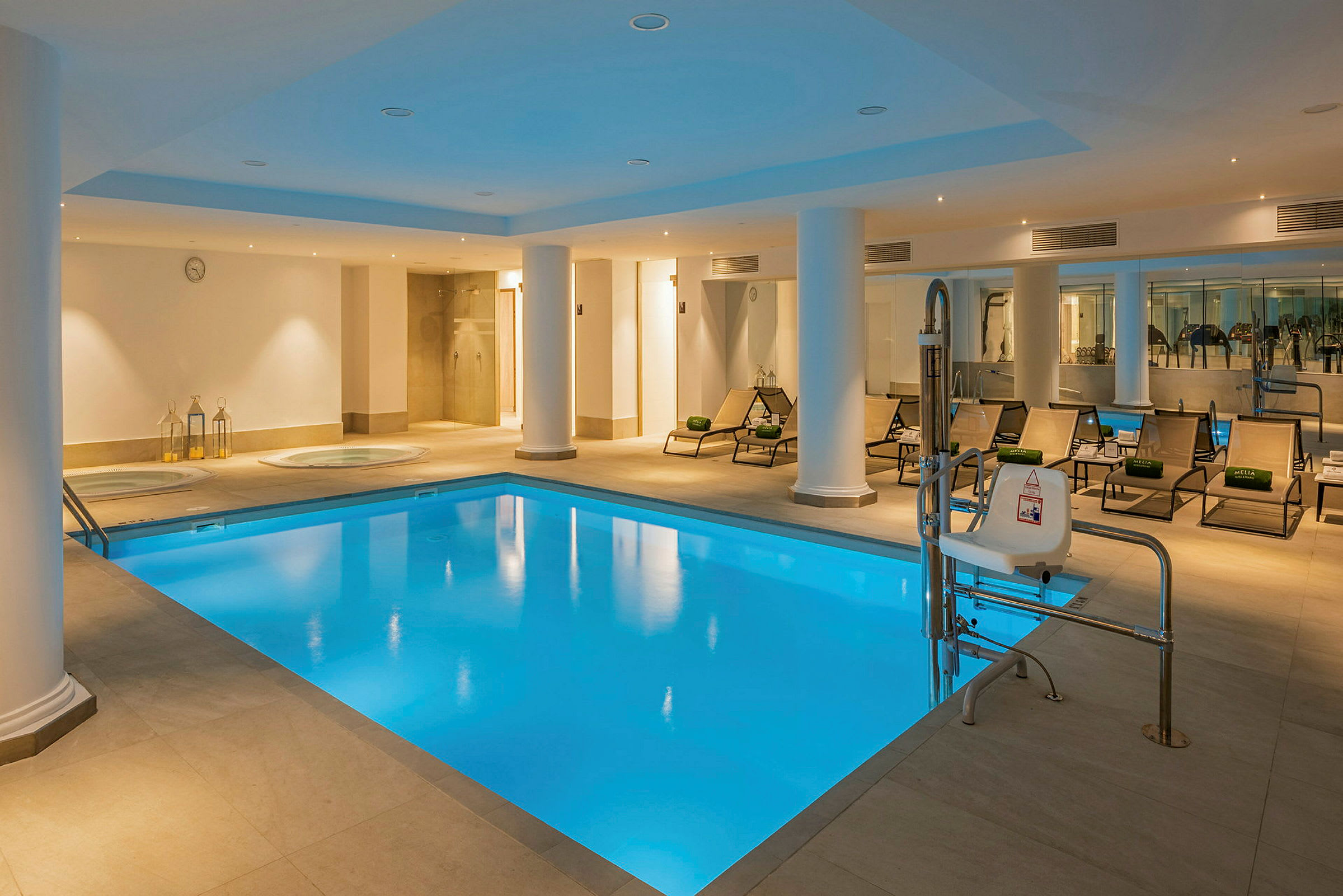 En inomhuspool med omgivande solstolar och pelare. I bakgrunden finns ett wellness-område. (AI-genererad text)