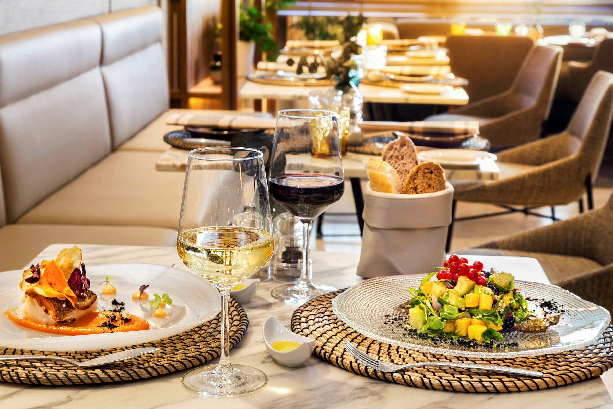 Ett dukat bord på en restaurang med två tallrikar mat, vinglas och en brödkorg. (AI-genererad text)