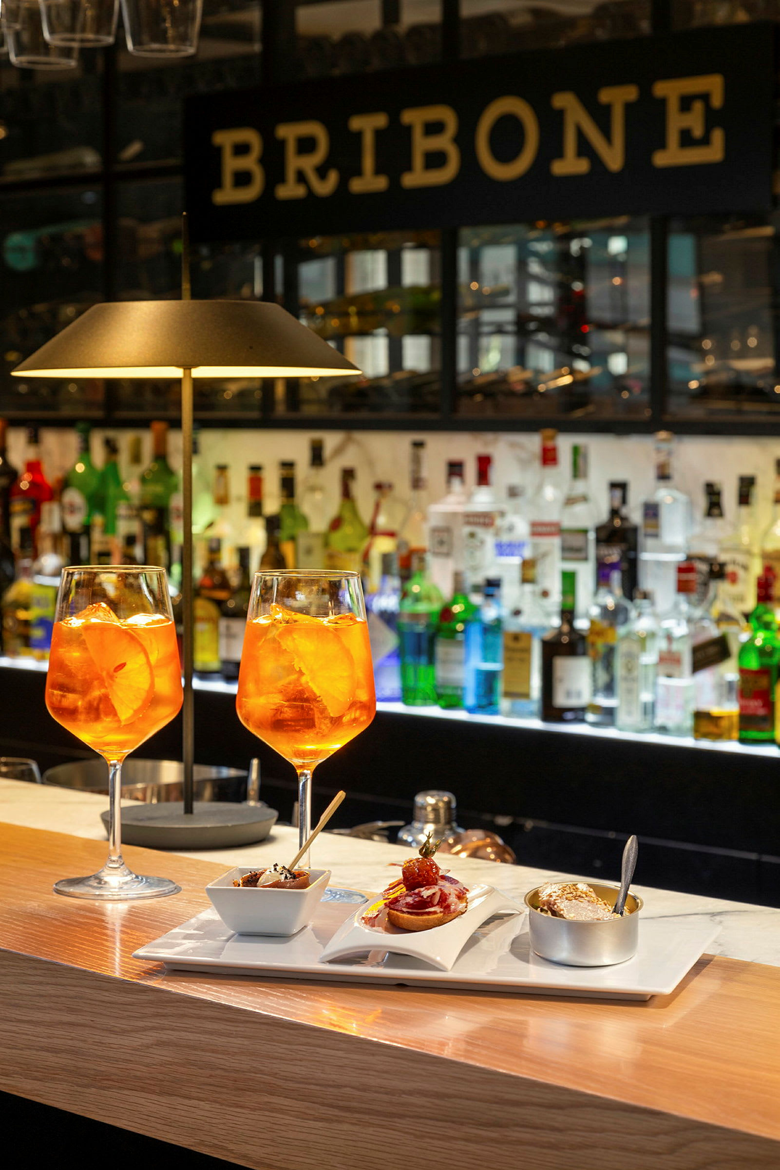 Två glas med orange dryck och en tallrik med olika små rätter står på en bardisk. (AI-genererad text)