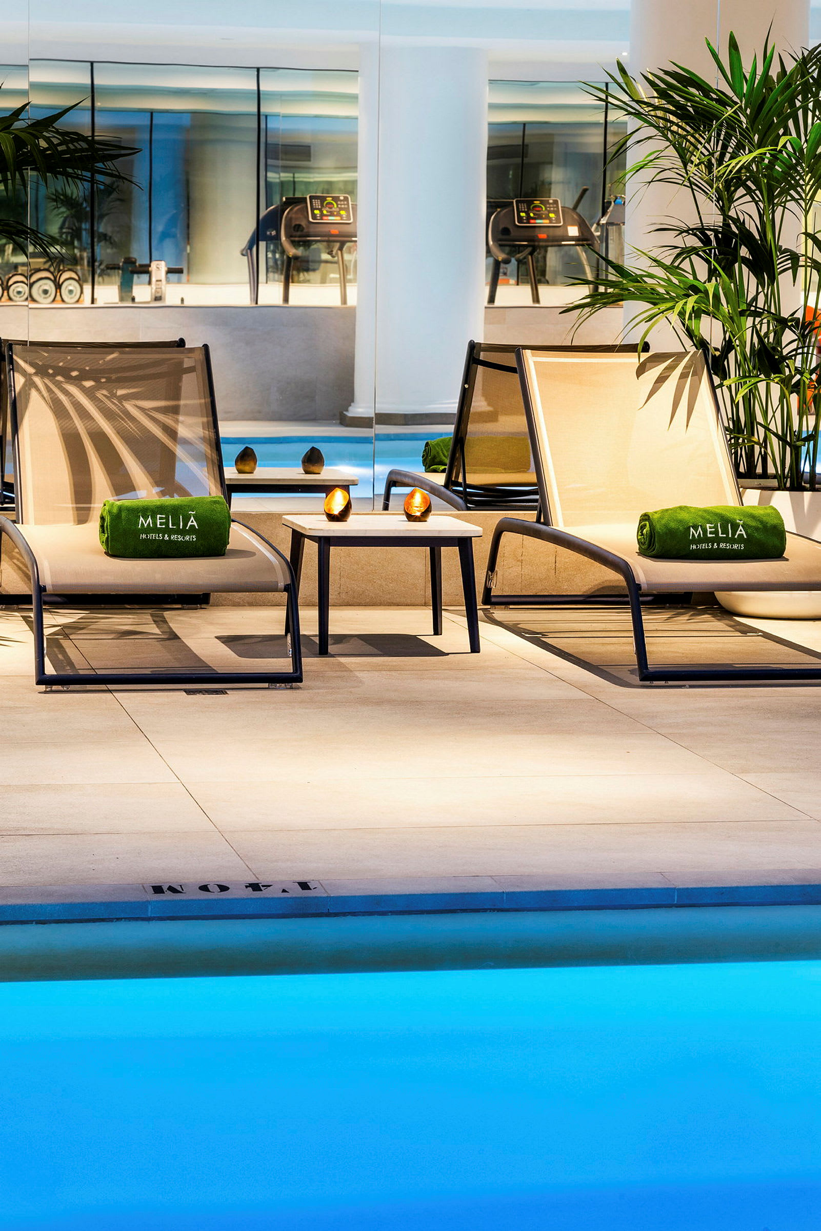 Två solstolar med gröna handdukar och ett litet bord står vid en inomhuspool i ett elegant spaområde. (AI-genererad text)