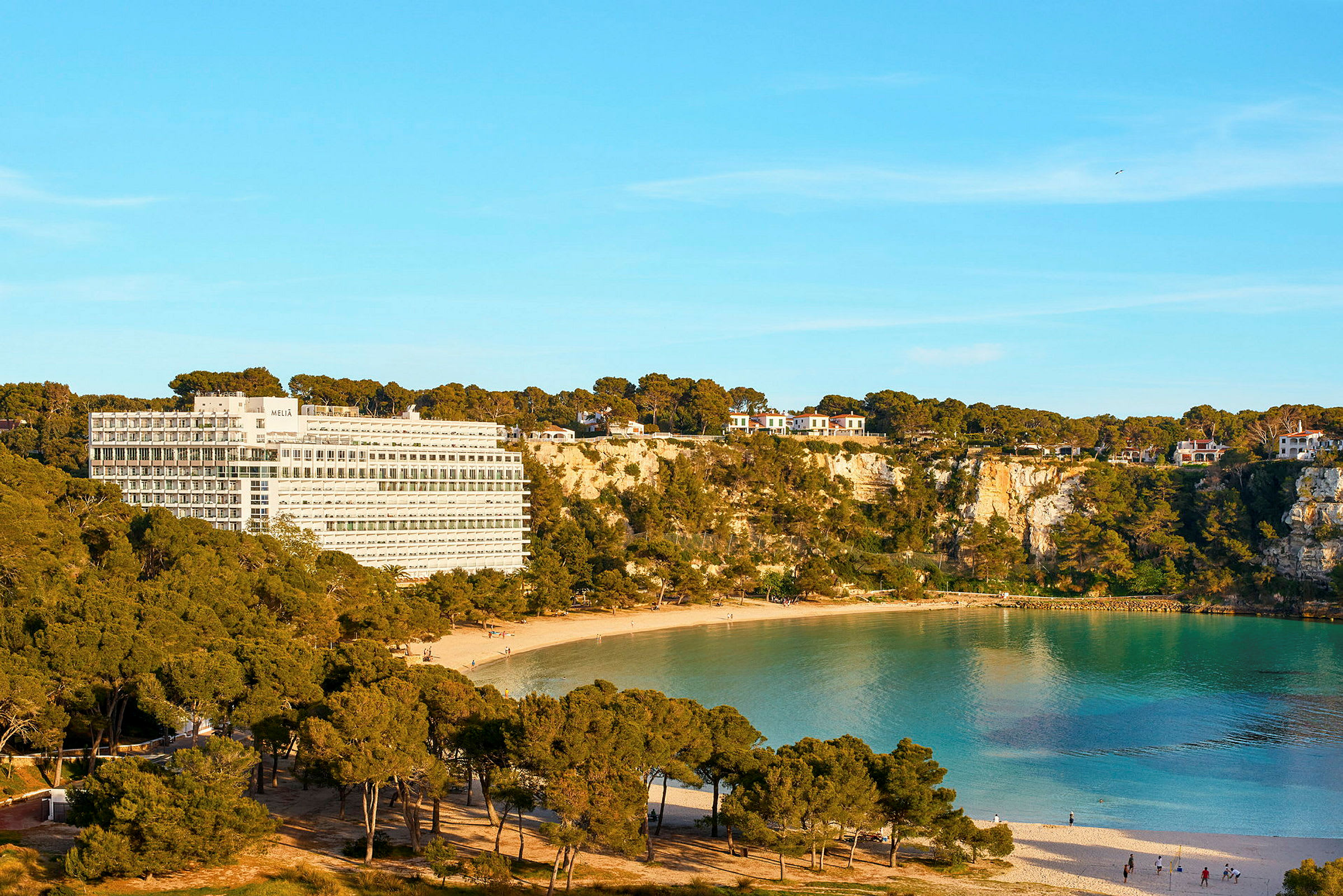 Hotellbyggnad vid en klippig kust med en sandstrand och turkost vatten. (AI-genererad text)