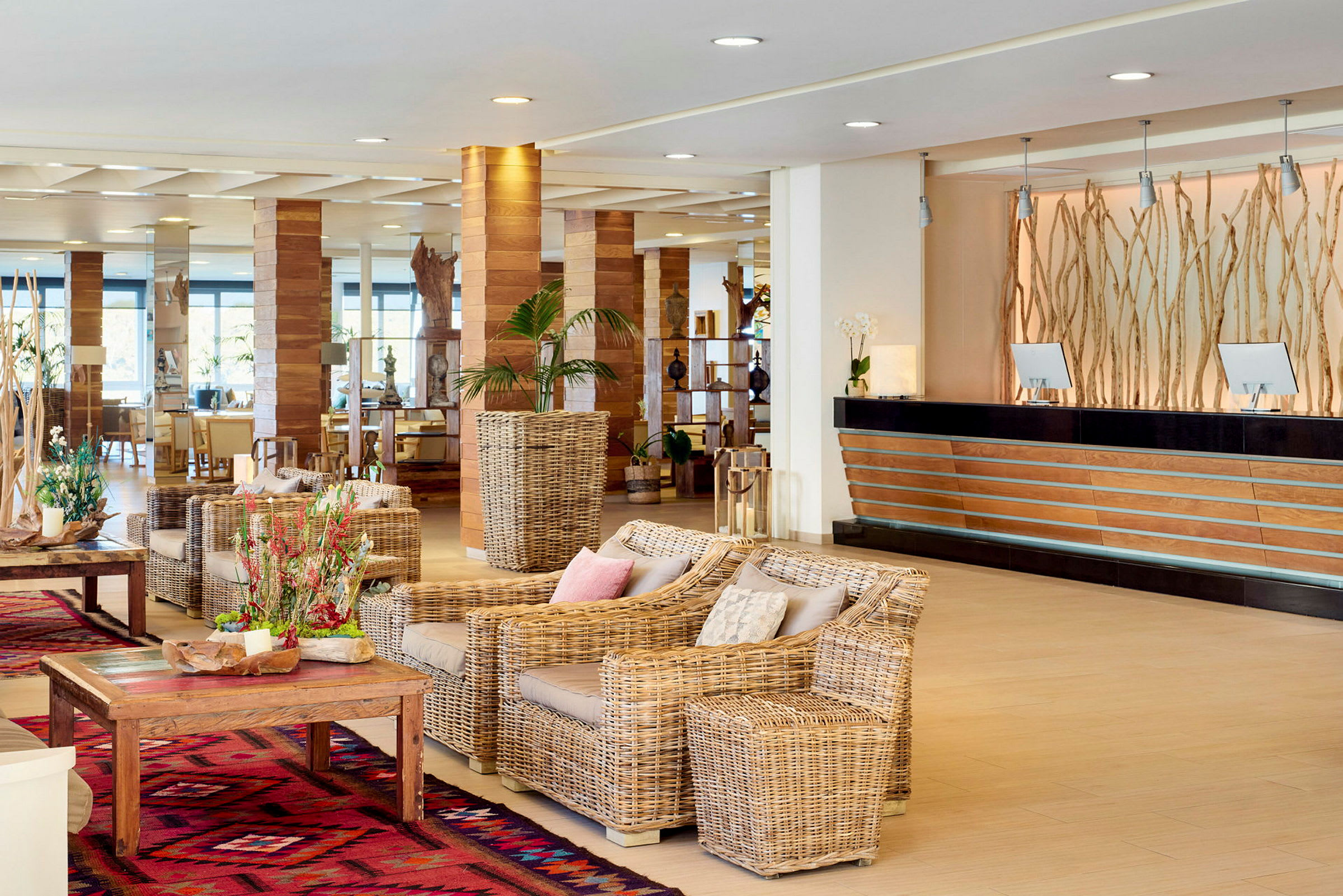 Ljust och öppet hotellobbyområde med sittgrupp av rottingmöbler och receptionsdisk i trä och svart. (AI-genererad text)