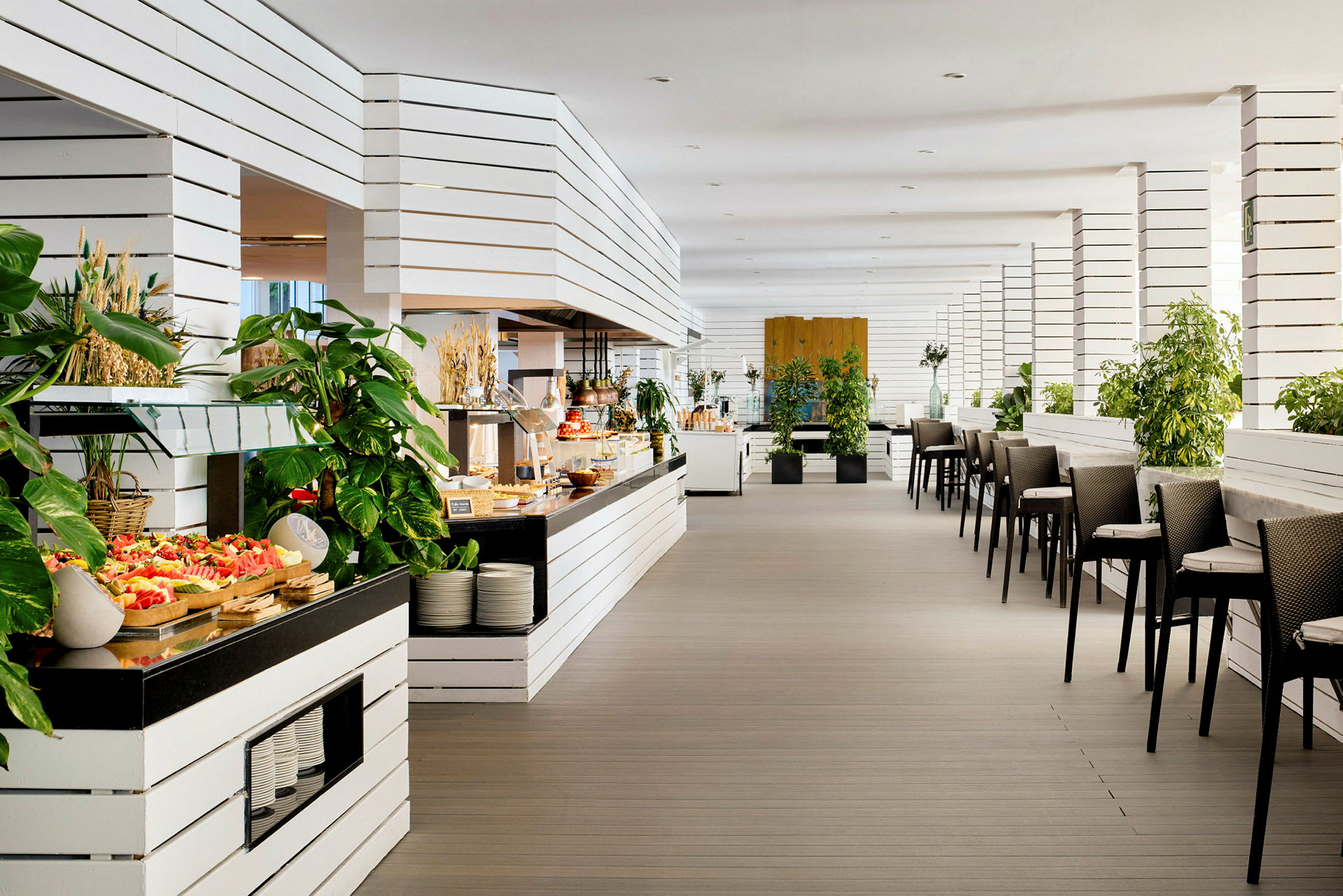 Inredning av en modern restaurang med vita träpaneler, gröna växter och serveringsbord fyllda med mat. (AI-genererad text)