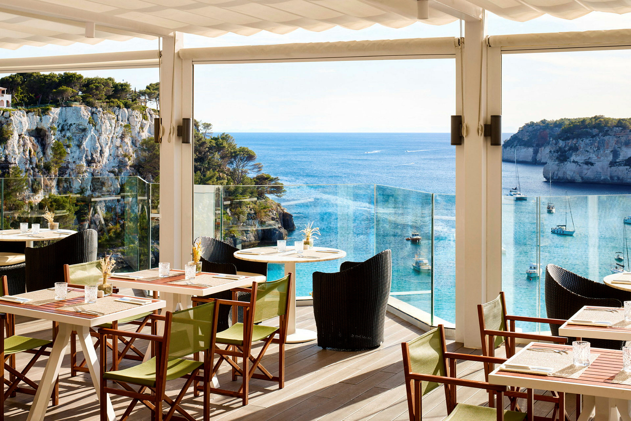 En restaurangterrass med bord och stolar, som har utsikt över havet och klippor. (AI-genererad text)