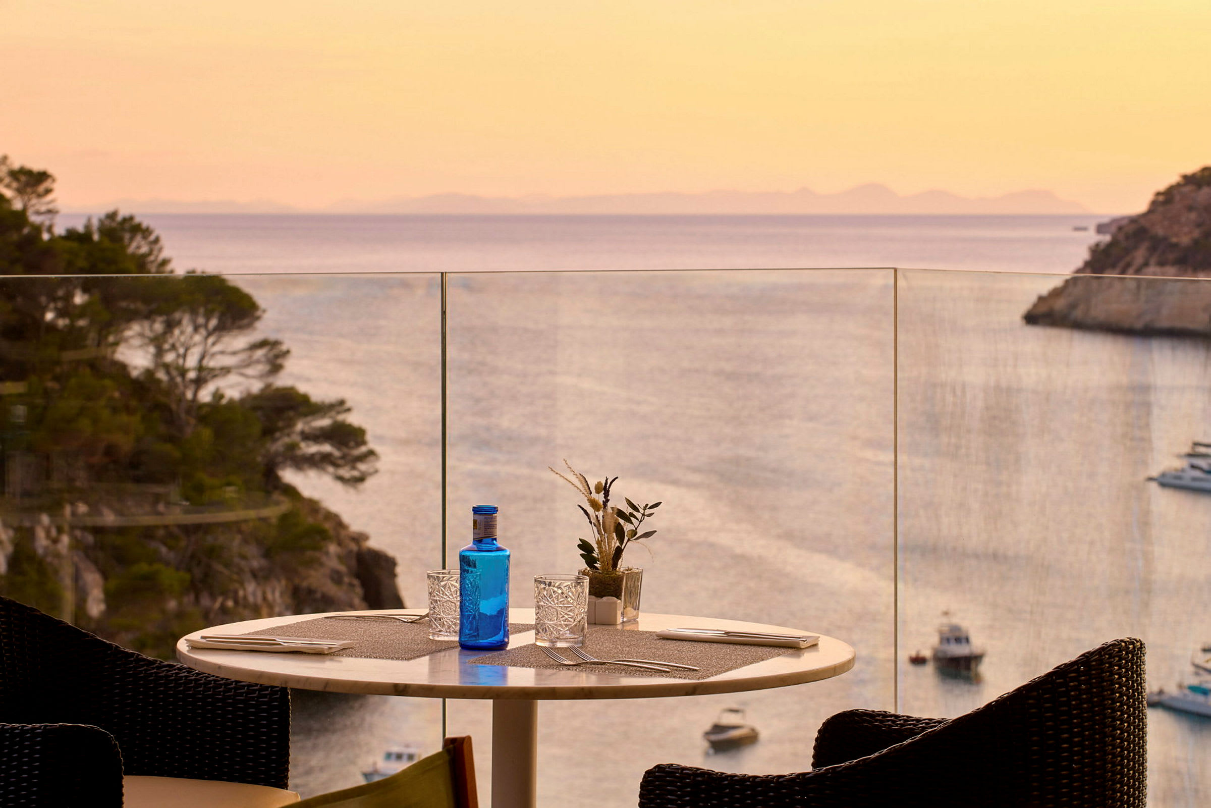 Ett dukat bord på en terrass med utsikt över havet och en solnedgång. (AI-genererad text)