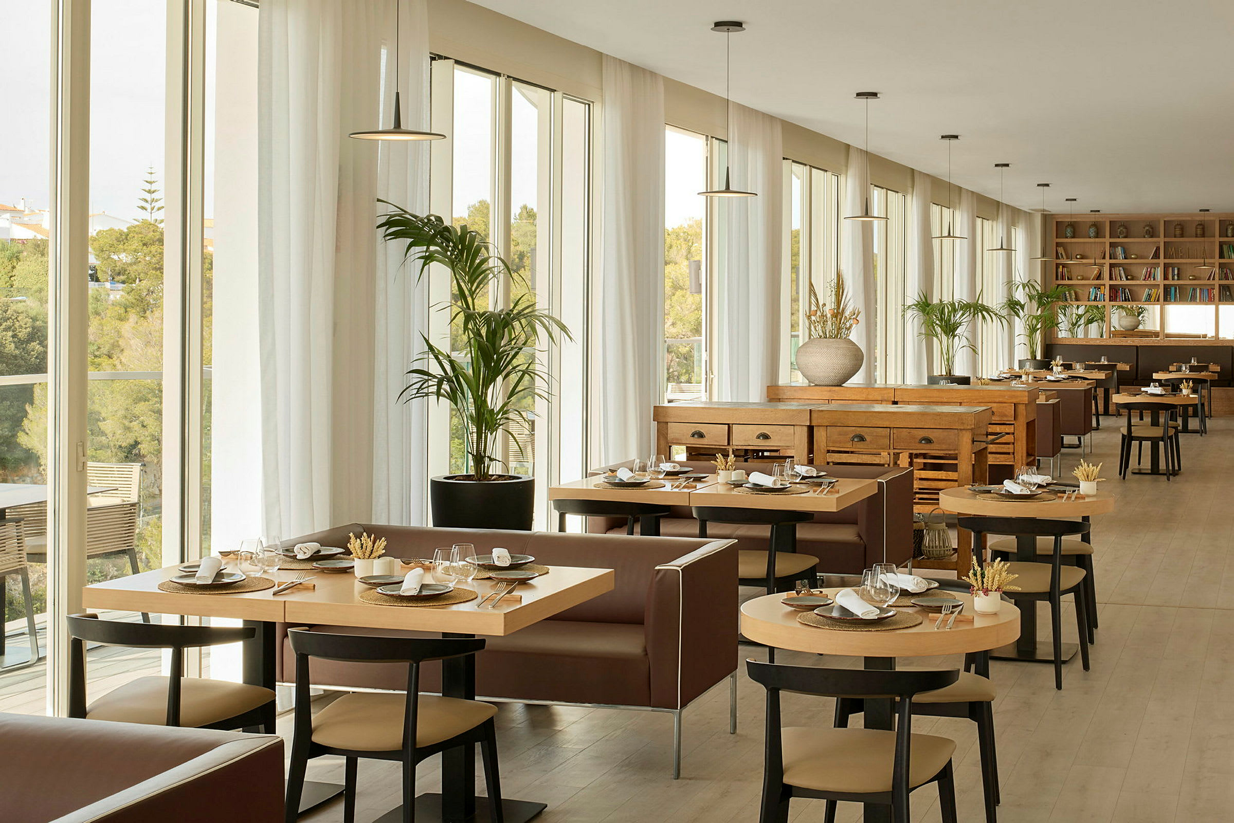 En ljus och rymlig restaurang med stora fönster, moderna möbler och bord som är dukade för måltider. (AI-genererad text)