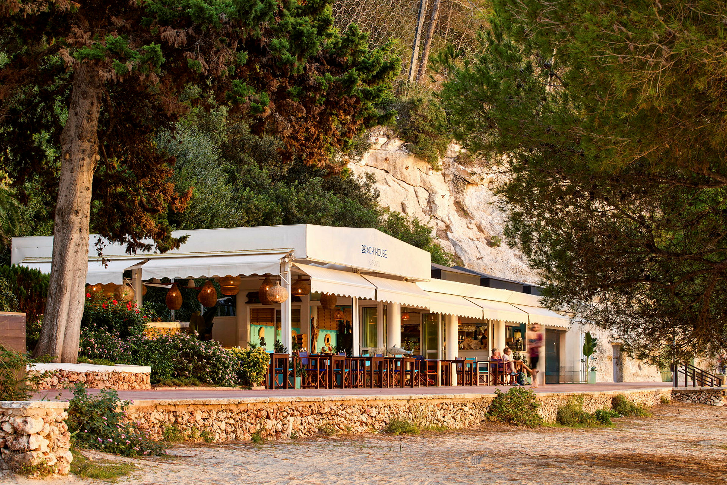 En strandnära restaurang med uteservering omgiven av träd och grönska. (AI-genererad text)