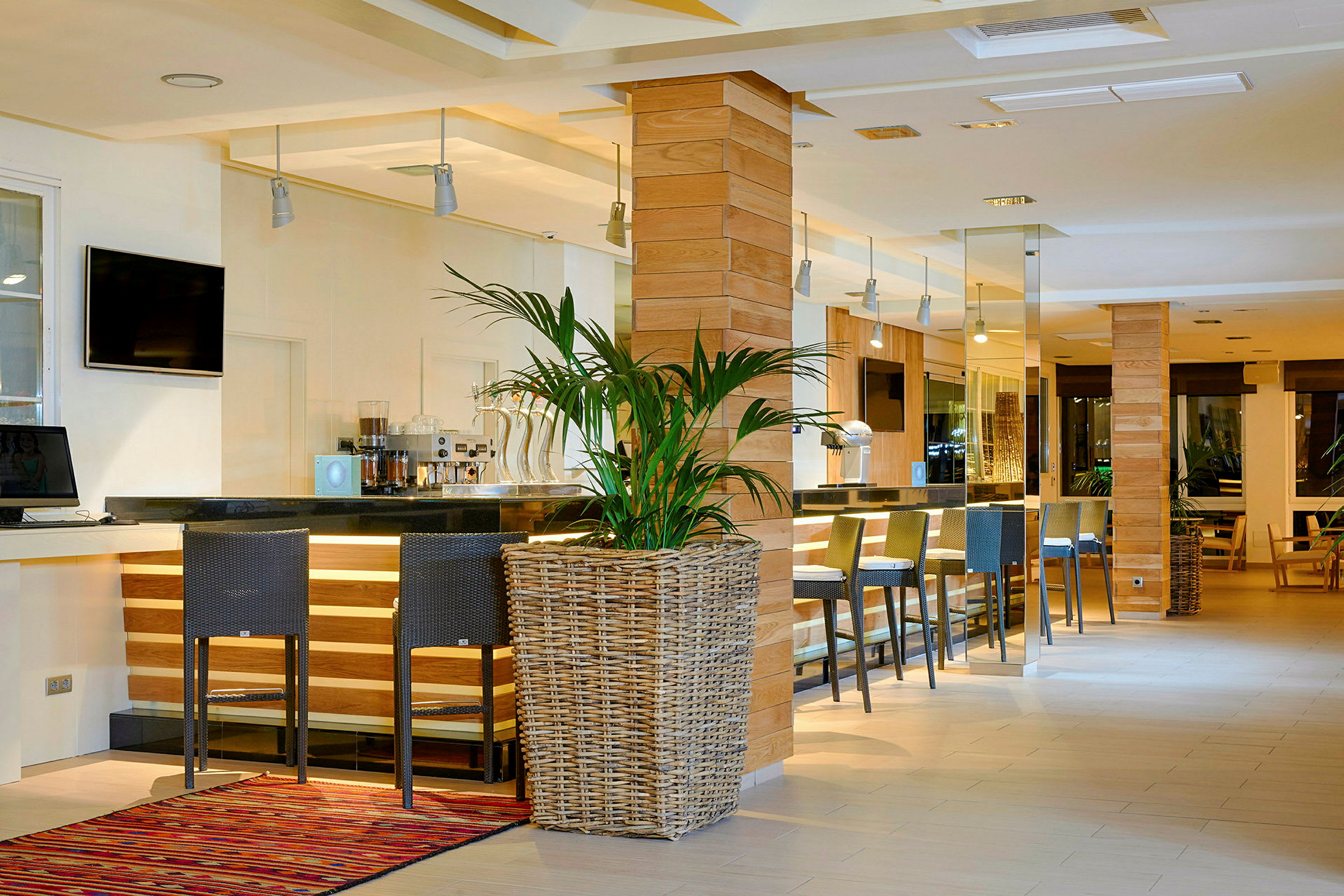 Bild av en modern och stilfull hotellbar med höga stolar, en bardisk i svart, träpaneler och en stor krukväxt i förgrunden. (AI-genererad text)