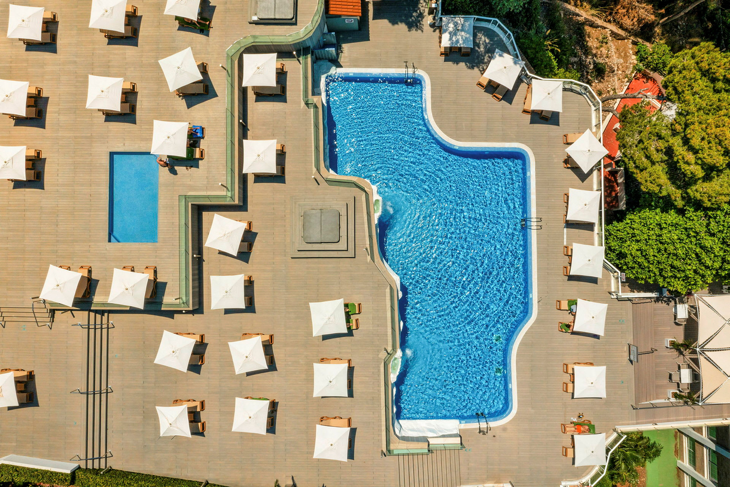 Flygvy av en pool omgiven av löparbanor och solstolar med vita parasoller. (AI-genererad text)