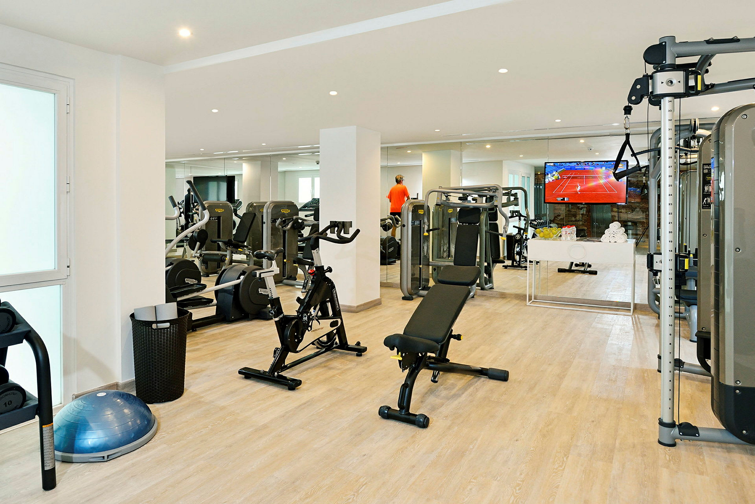 Ett gym med träningsutrustning som cyklar, bänkar och maskiner, samt en TV på väggen. (AI-genererad text)