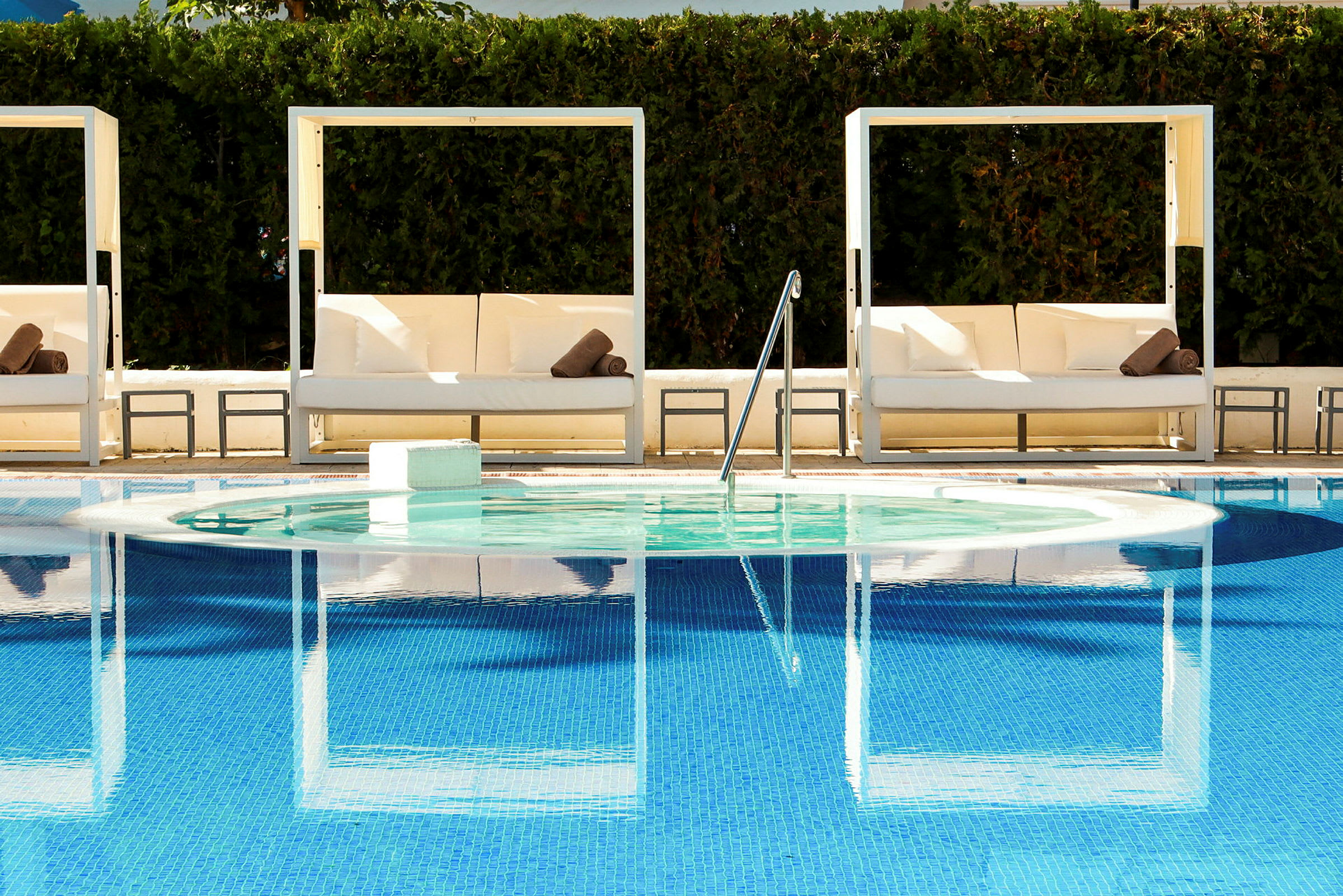 Utemöbler och glasstolar vid en pool med spegelblått vatten. (AI-genererad text)
