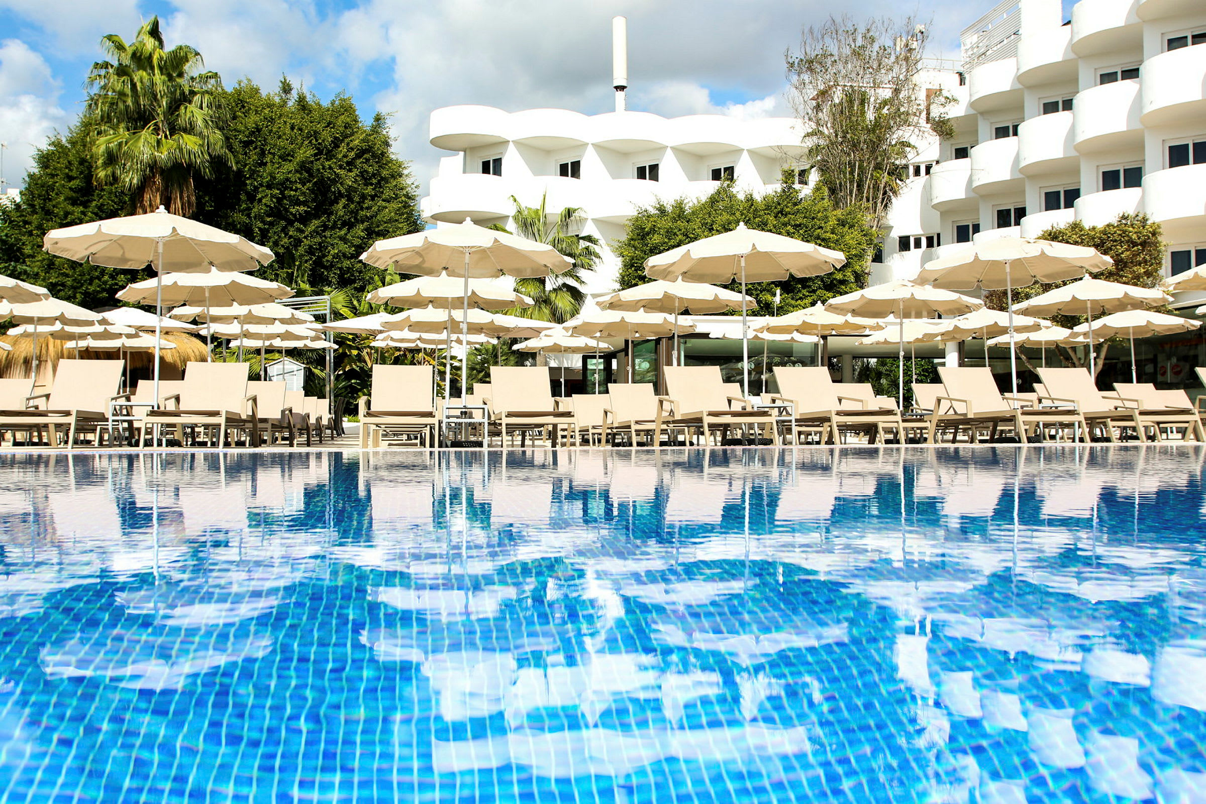 En pool med solstolar och parasoller framför ett hotell. (AI-genererad text)