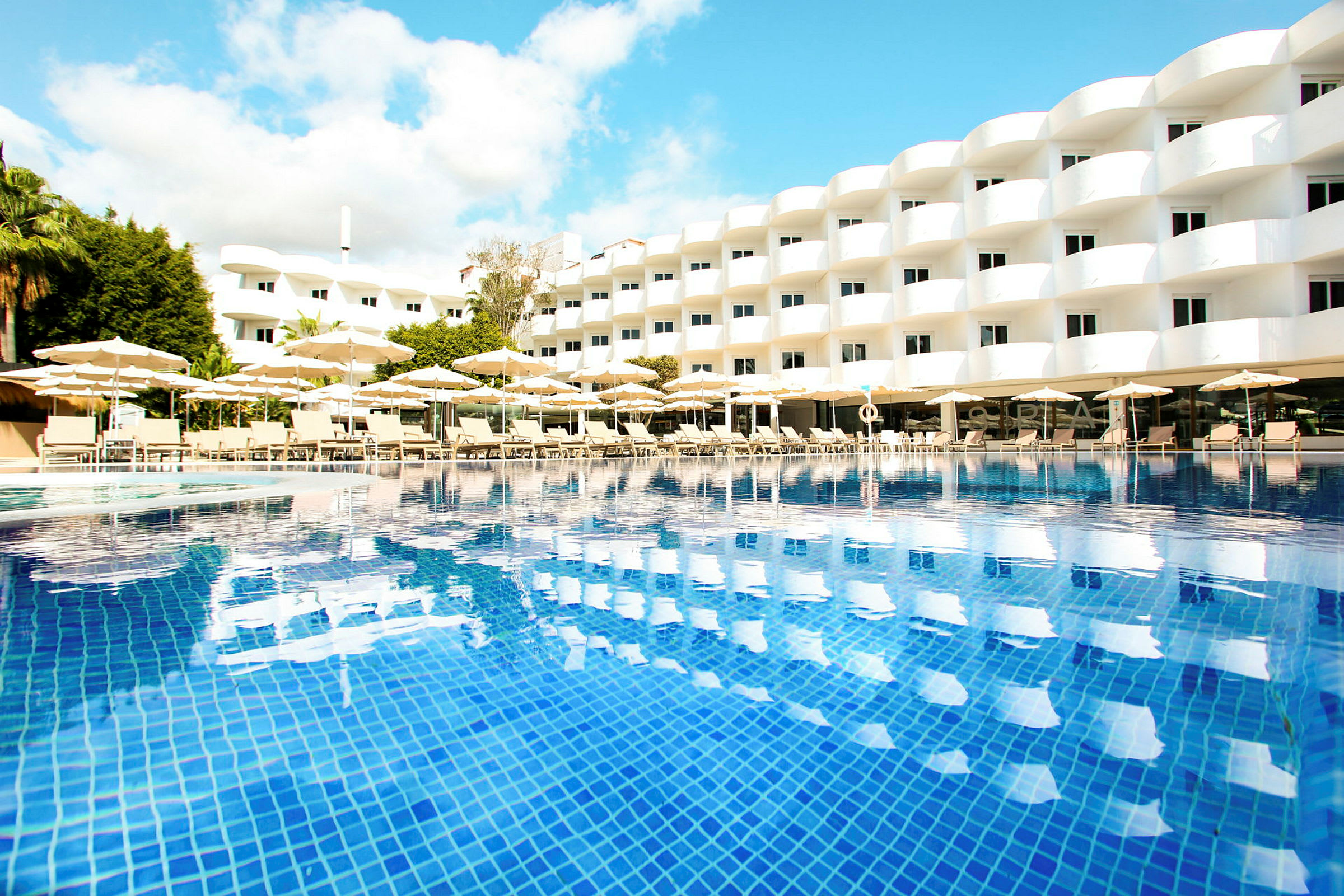 Ett modernt hotell med bländvita fasader, solstolar och parasoll vid en klarblå pool. (AI-genererad text)