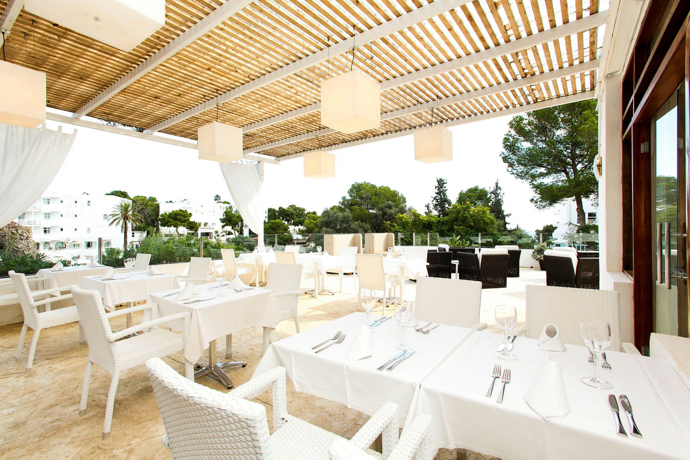 En terrass med bord och stolar, dukade för måltid, under en pergola. (AI-genererad text)