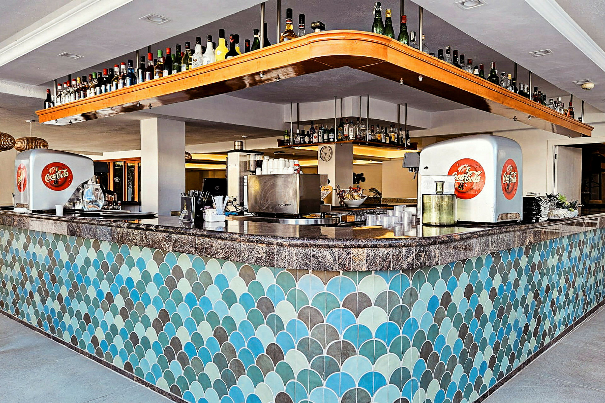 En bar med blå och gröna kakelplattor på fronten och flaskor på hyllor ovanför. (AI-genererad text)