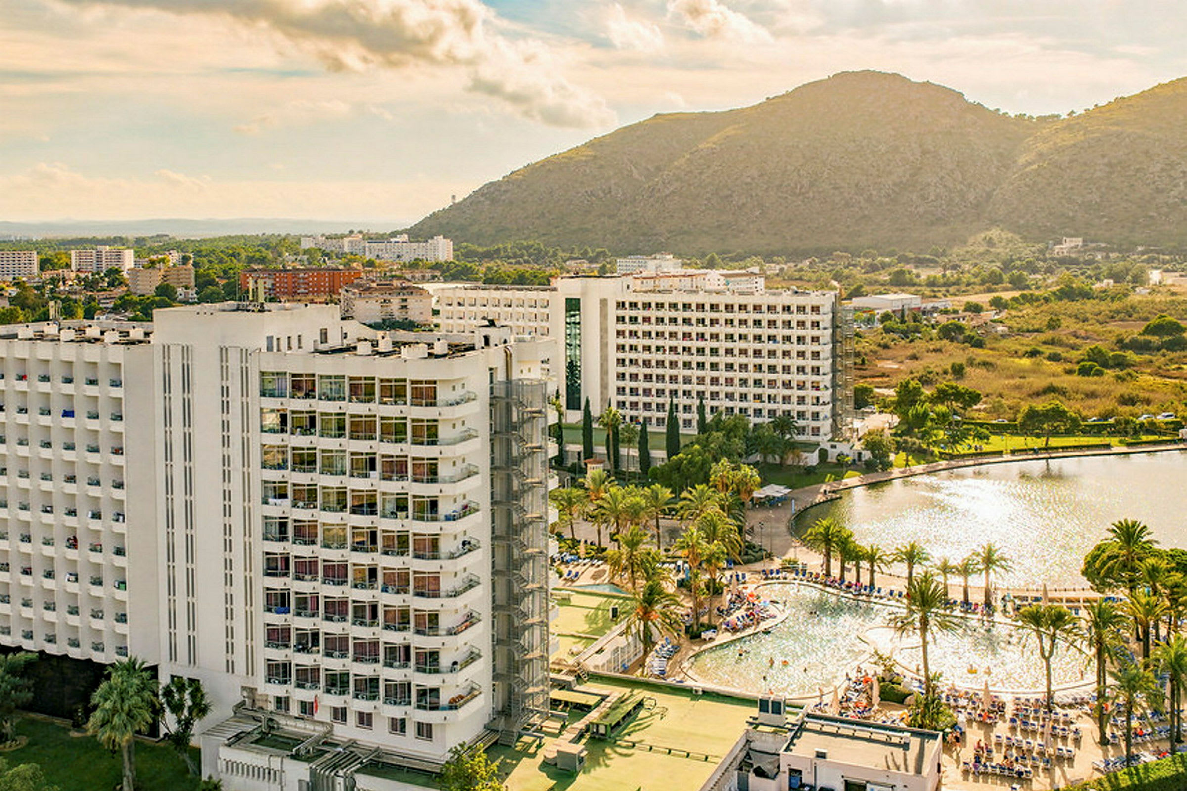 Bild av ett hotell med omgivande poolområde, palmer och berg i bakgrunden. (AI-genererad text)