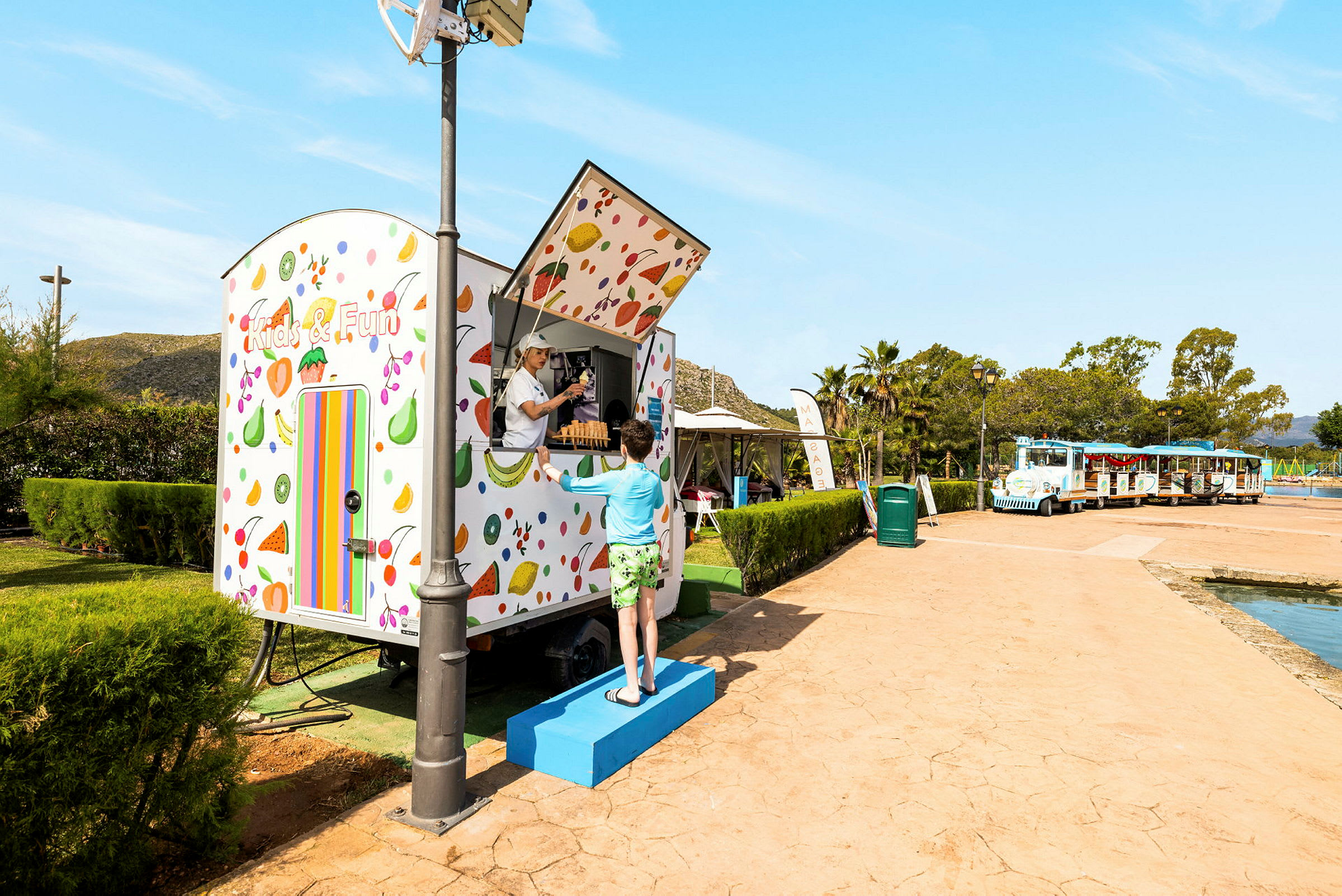 En färgglad kiosk med texten "Kids & Fun". En person står framför och samtalar med personal i kiosken. (AI-genererad text)