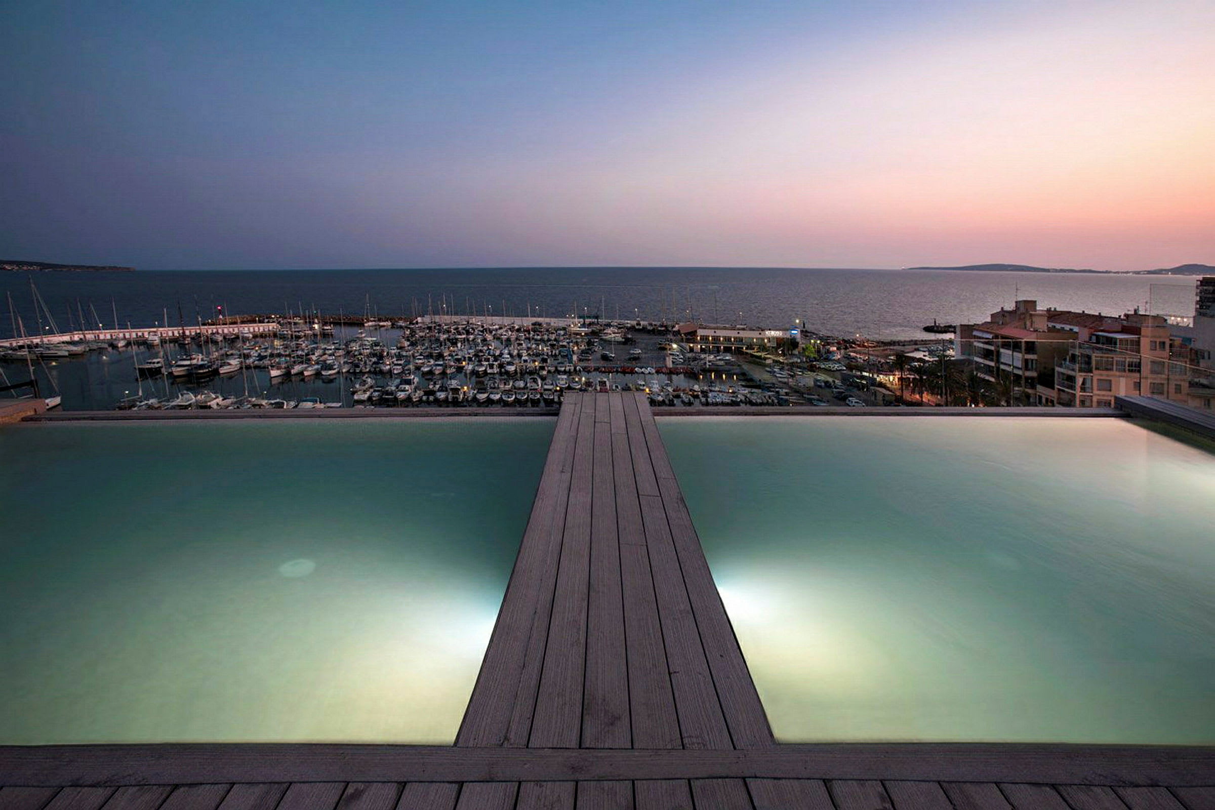 En infinitypool med utsikt över en marina och havet vid solnedgången. (AI-genererad text)