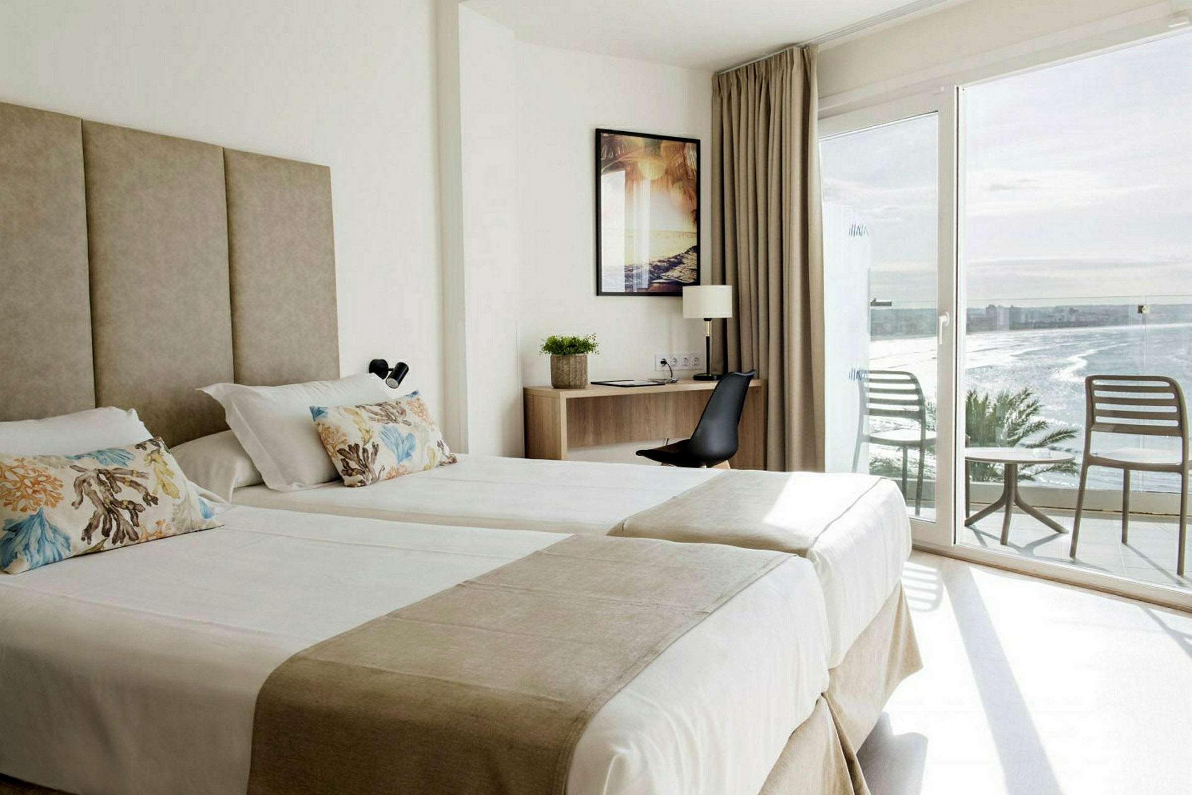 Hotellrum med två enkelsängar, skrivbord och två stolar på balkongen med havsutsikt. (AI-genererad text)