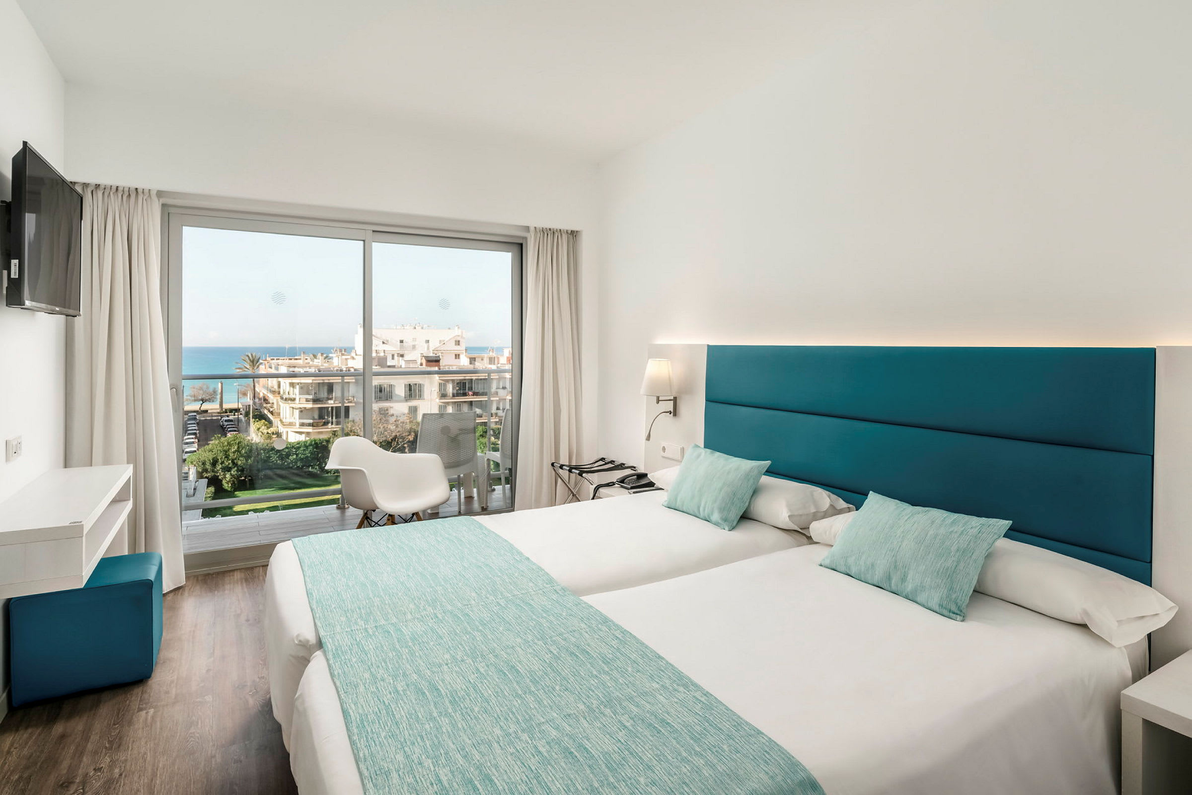 Ett ljust hotellrum med två enkelsängar, stora fönster och utsikt över havet. (AI-genererad text)