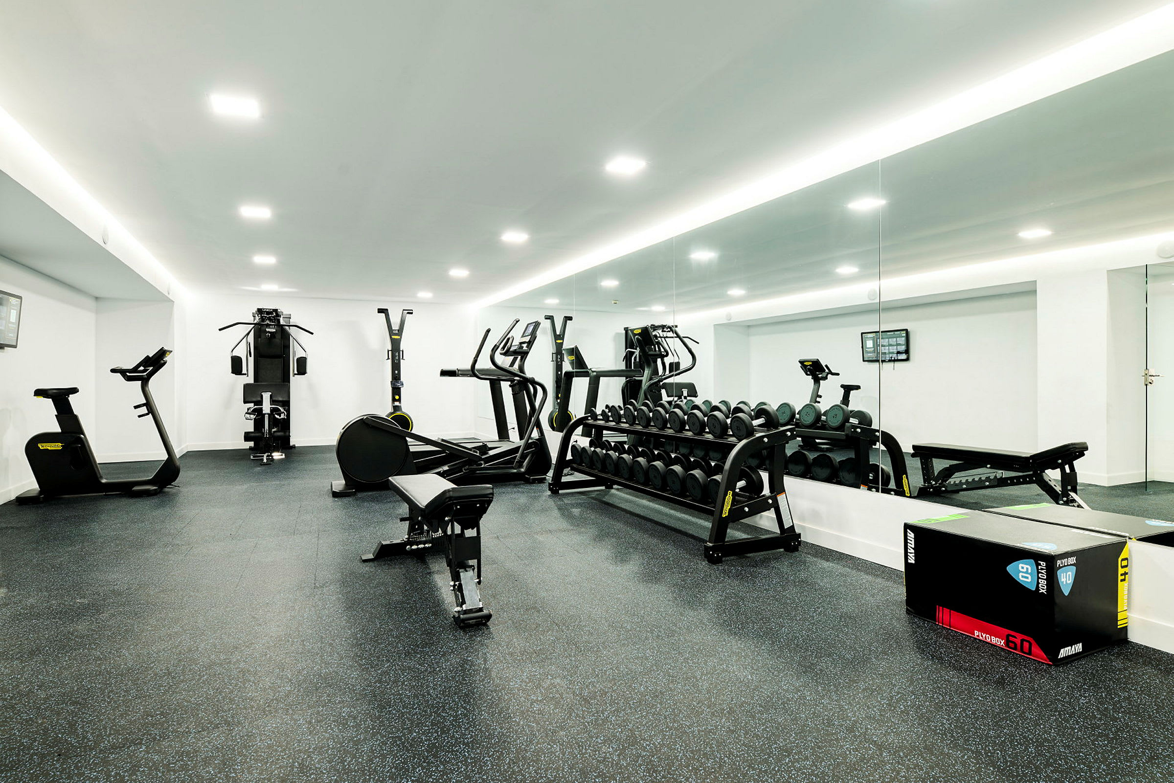 Ett gym med träningsmaskiner, fria vikter och spegelvägg. (AI-genererad text)