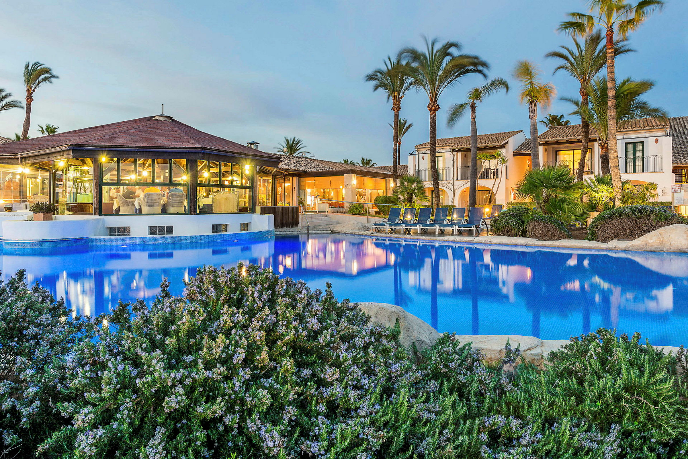 En hotellbyggnad med pool och solstolar omgiven av palmer. (AI-genererad text)