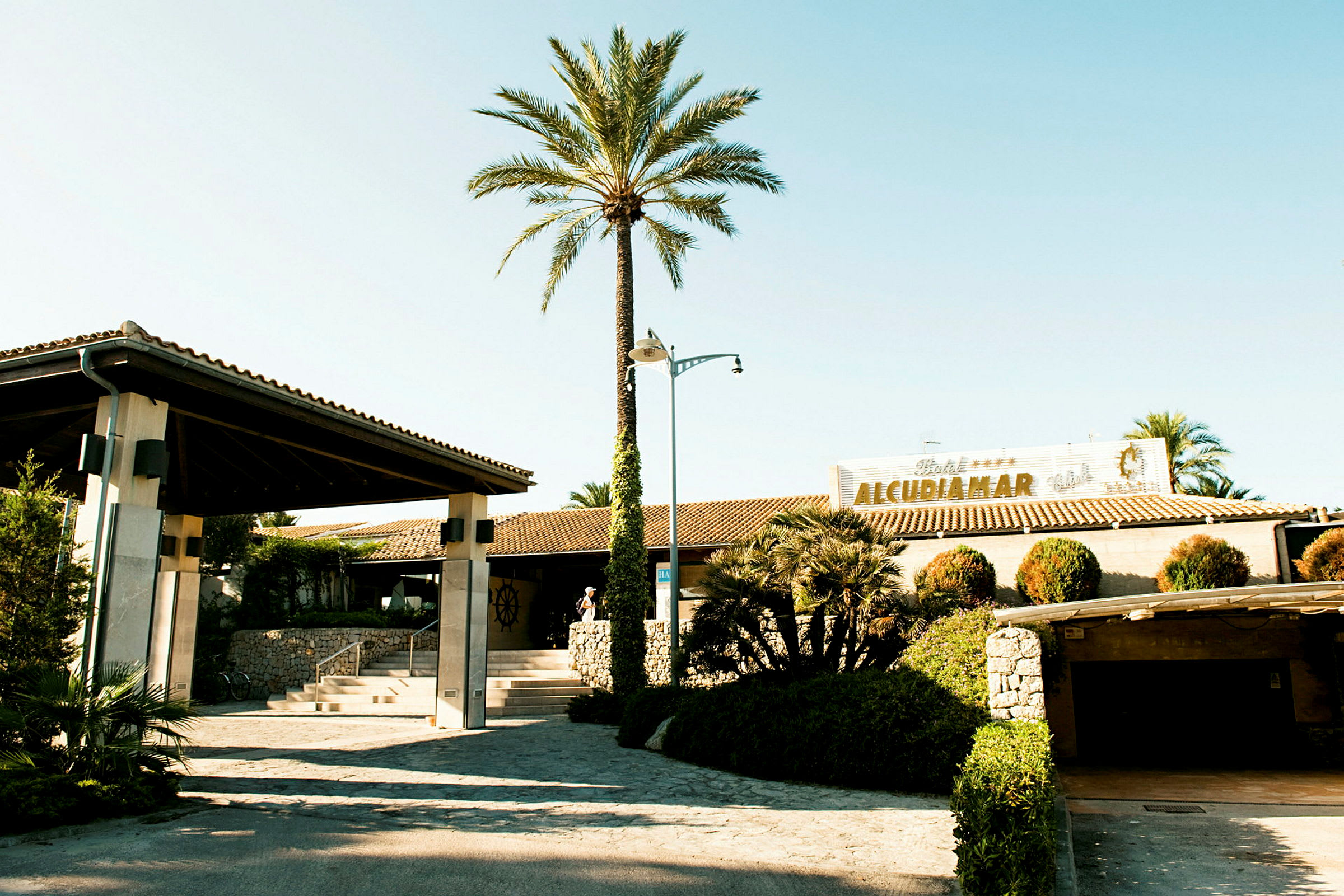 Hotell Alcudiamars entré omgiven av trädgård och palmer. (AI-genererad text)
