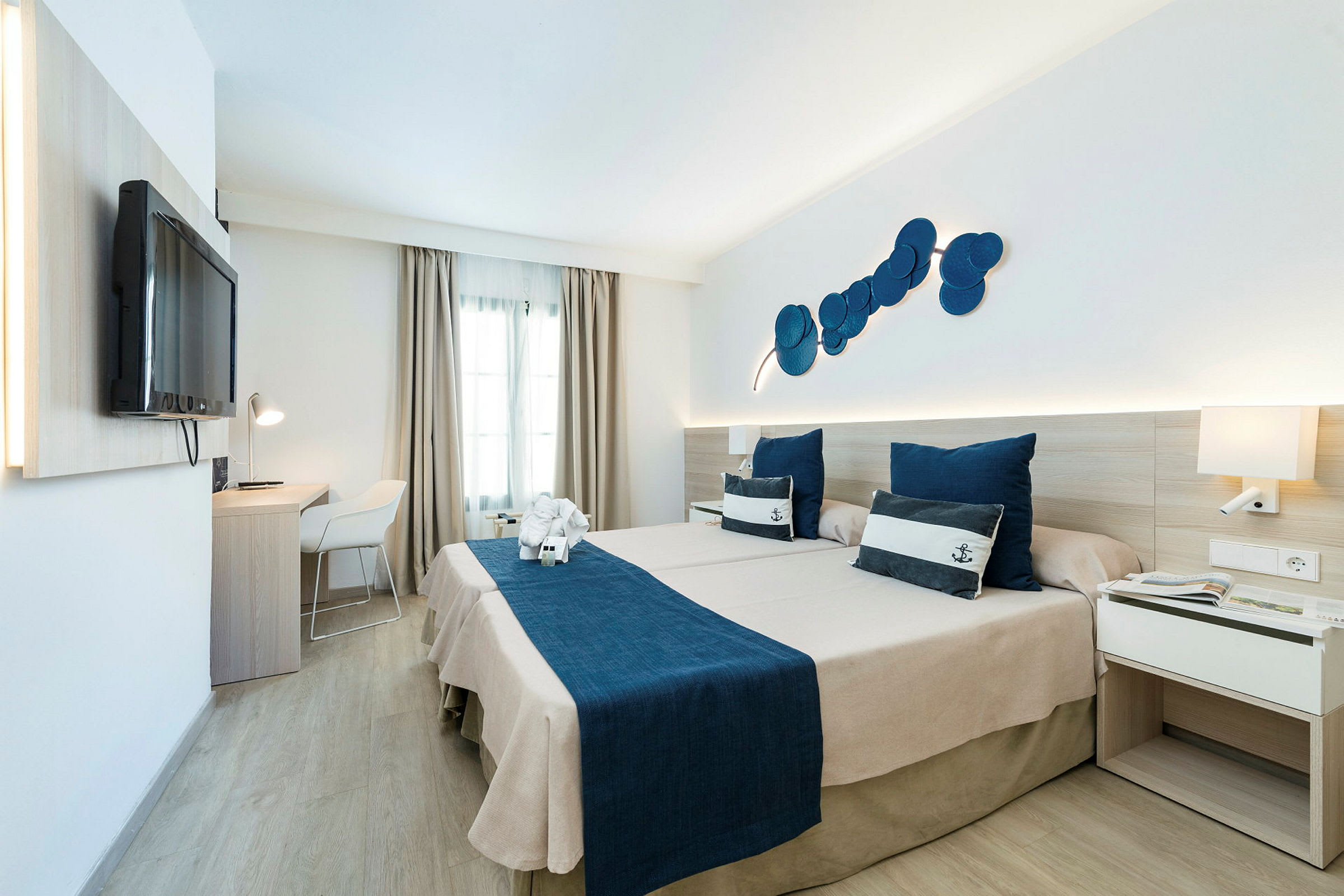 Hotellrum med två sängar och marin-tema, blå sängkläder och prydnadskuddar. (AI-genererad text)