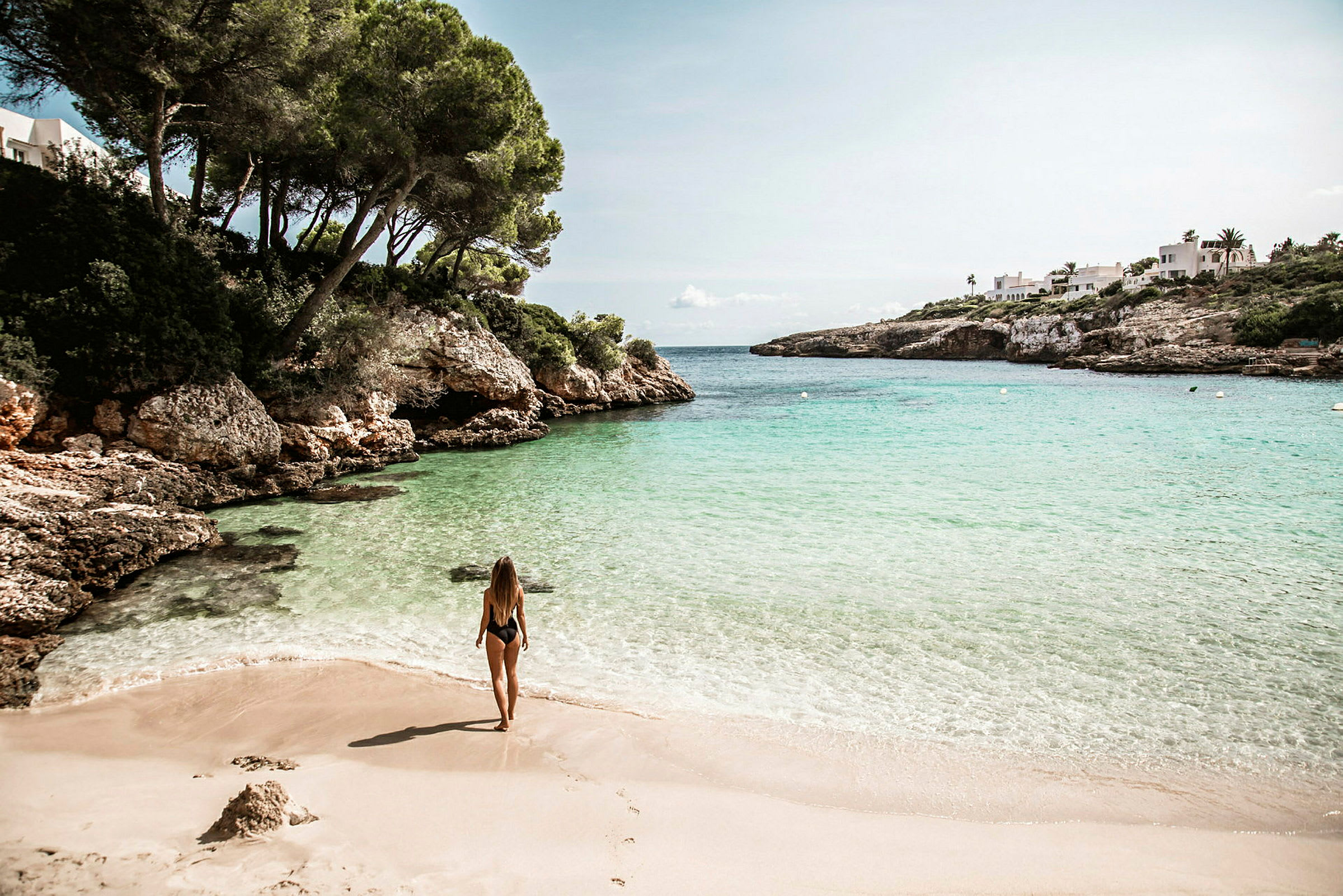 En kvinna står på en sandstrand med klarblått hav och klippformationer i bakgrunden. (AI-genererad text)