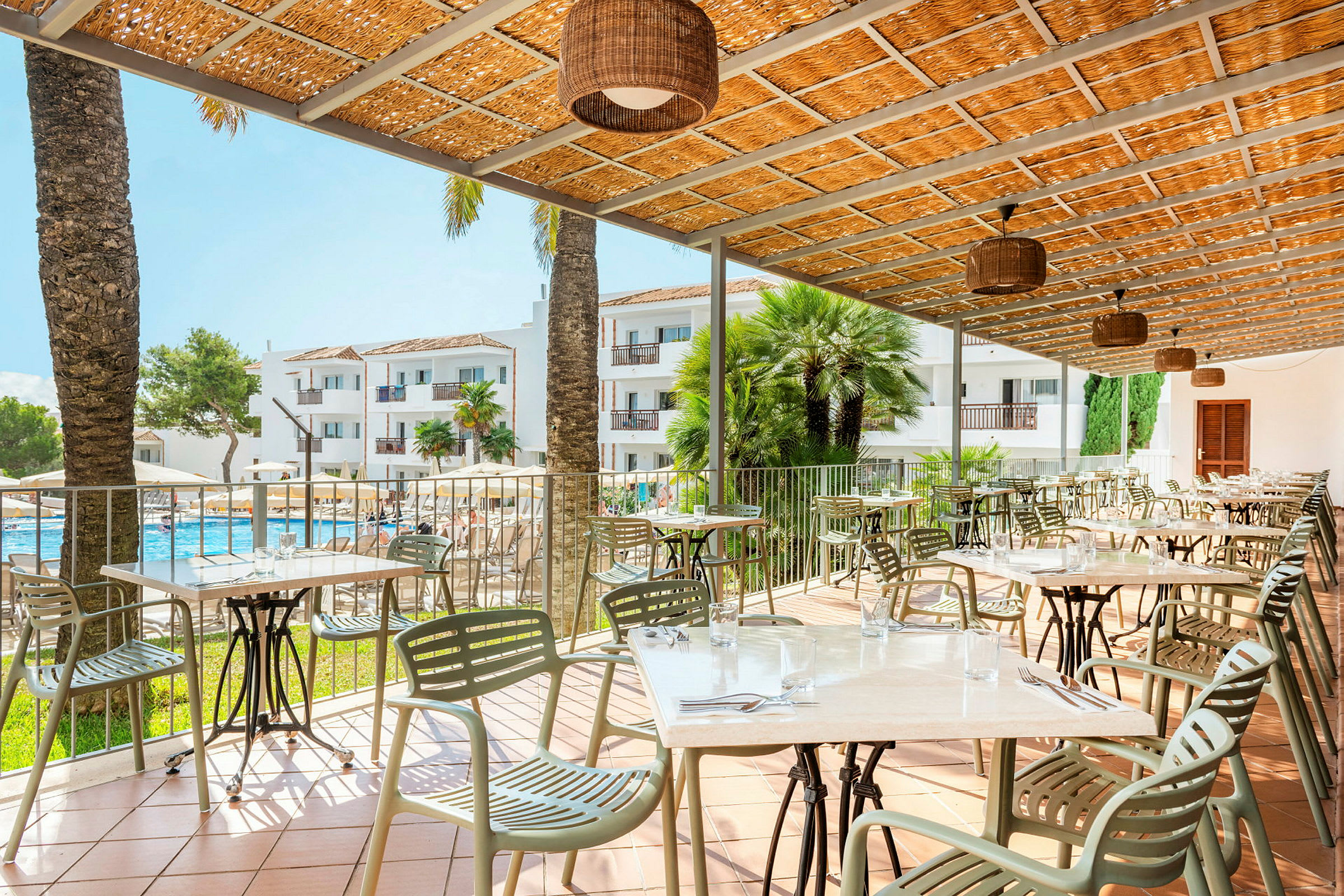 Terrass med bord och stolar, en pool och hotellbyggnader i bakgrunden. (AI-genererad text)