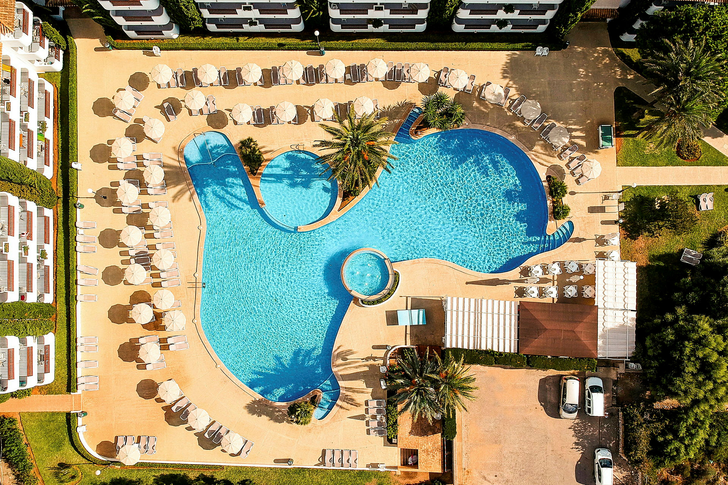 Flygfoto av en pool med solstolar och parasoller runtom. (AI-genererad text)