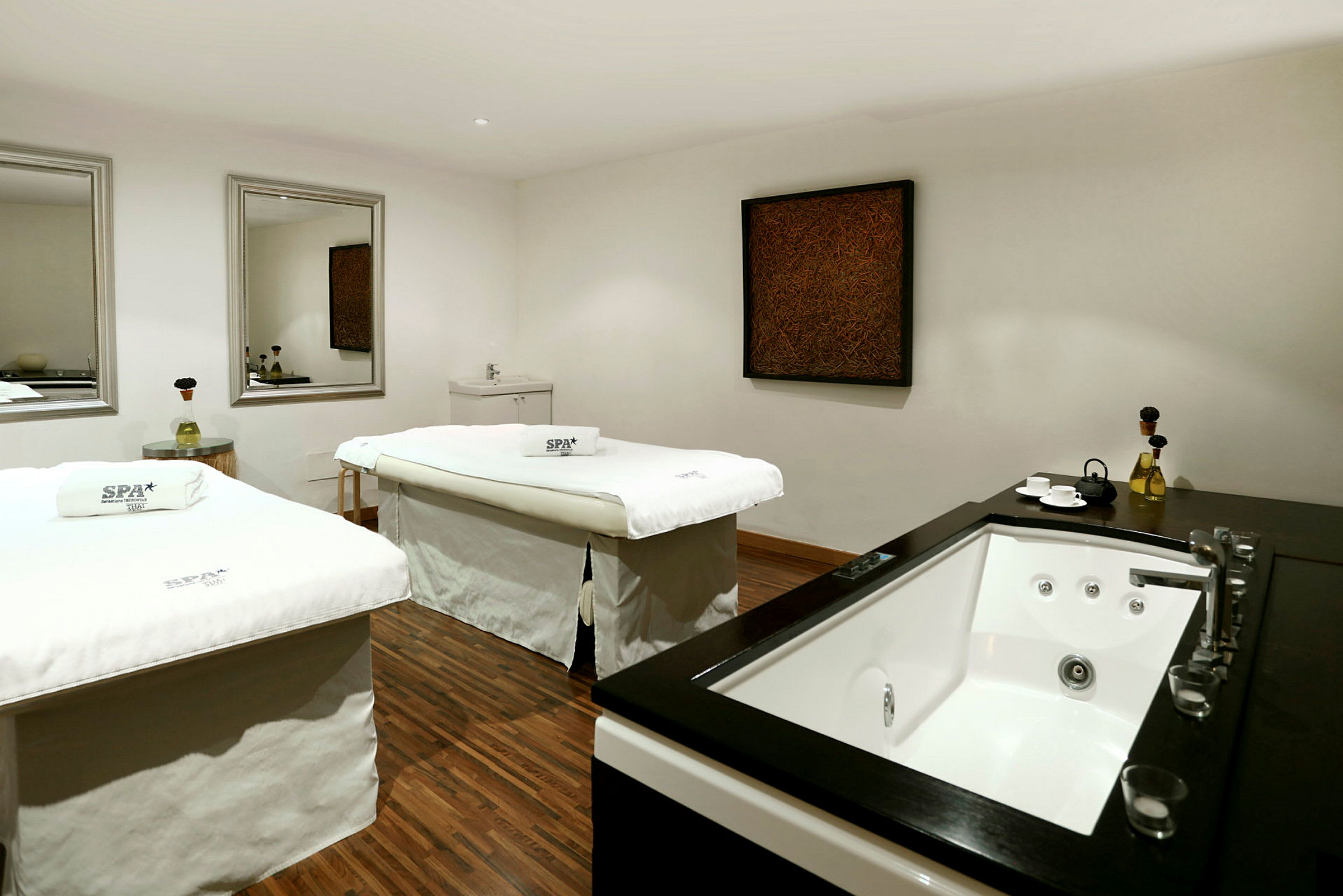 Rum med två spa-bänkar och en jacuzzi på sidan, inrett med speglar och konst på väggen. (AI-genererad text)