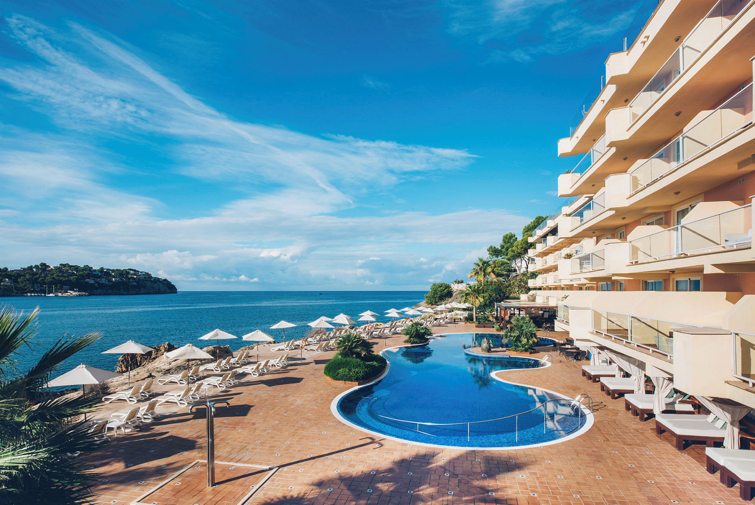 Bild av ett hotell vid havet med pool och solstolar. (AI-genererad text)