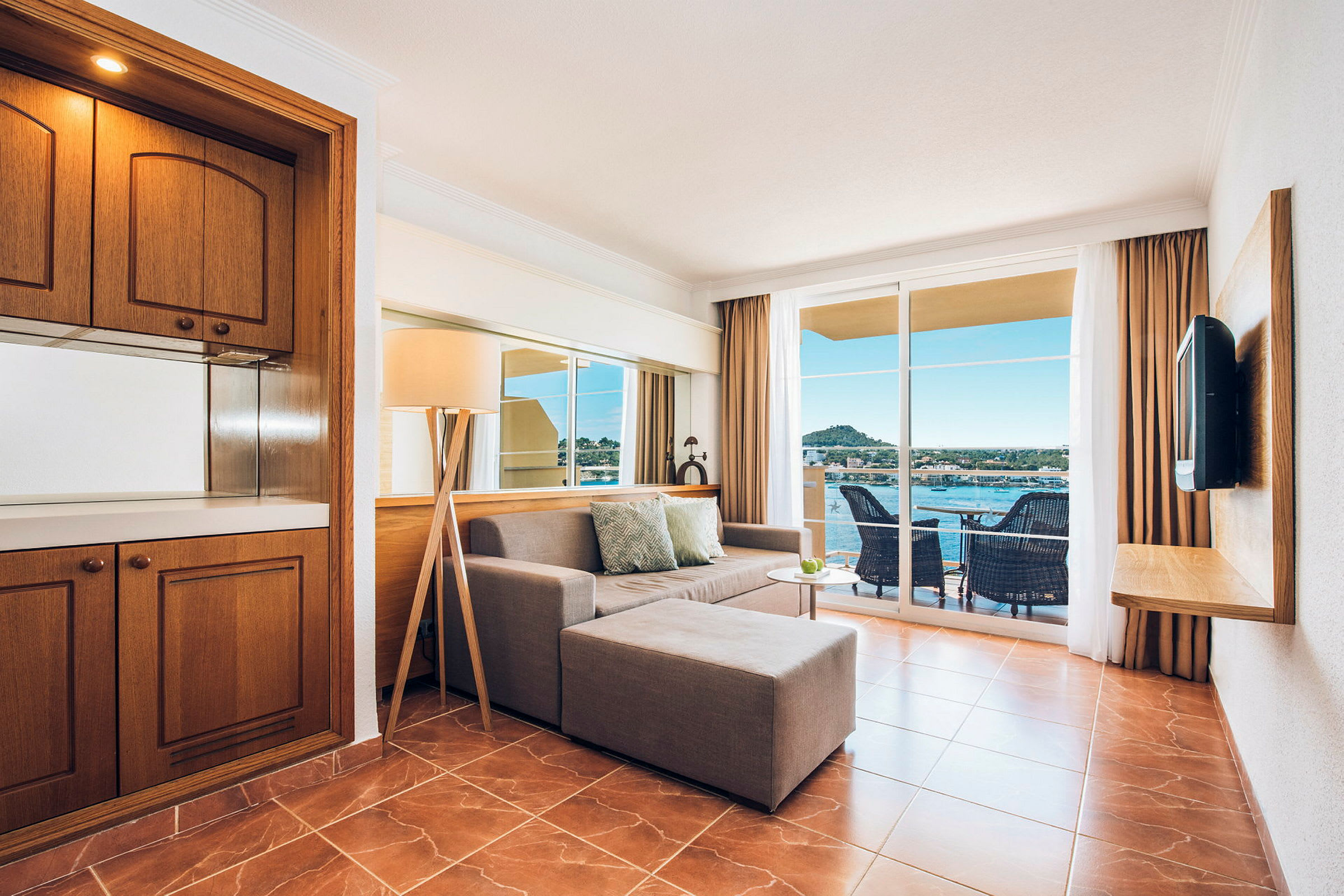 Ett hotellrum med soffa, soffbord och brunt golv. Stora fönster med utsikt över balkongen och havet. (AI-genererad text)