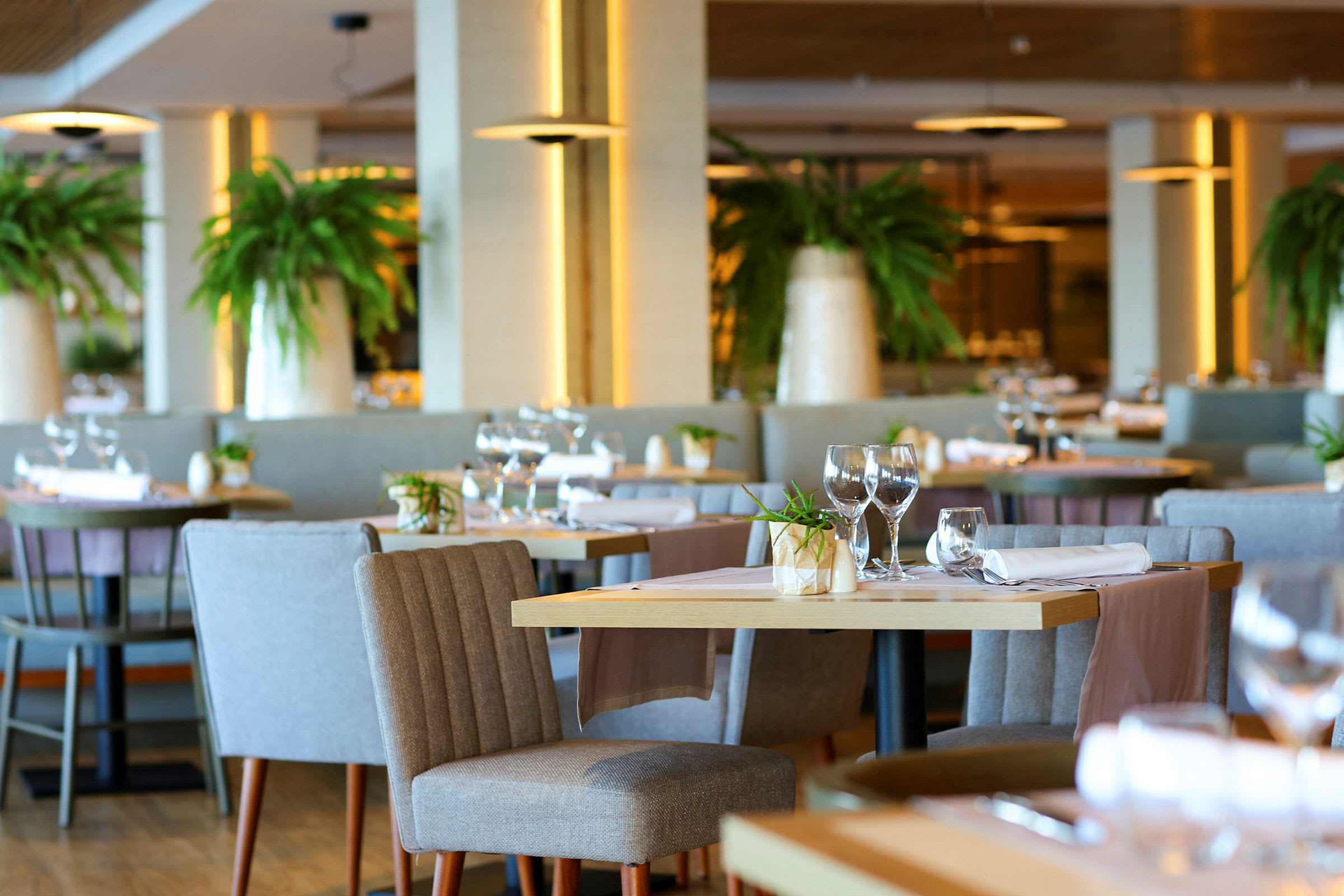Interiör av en elegant restaurang med dukade bord, bekväma stolar och gröna växter som dekoration. (AI-genererad text)