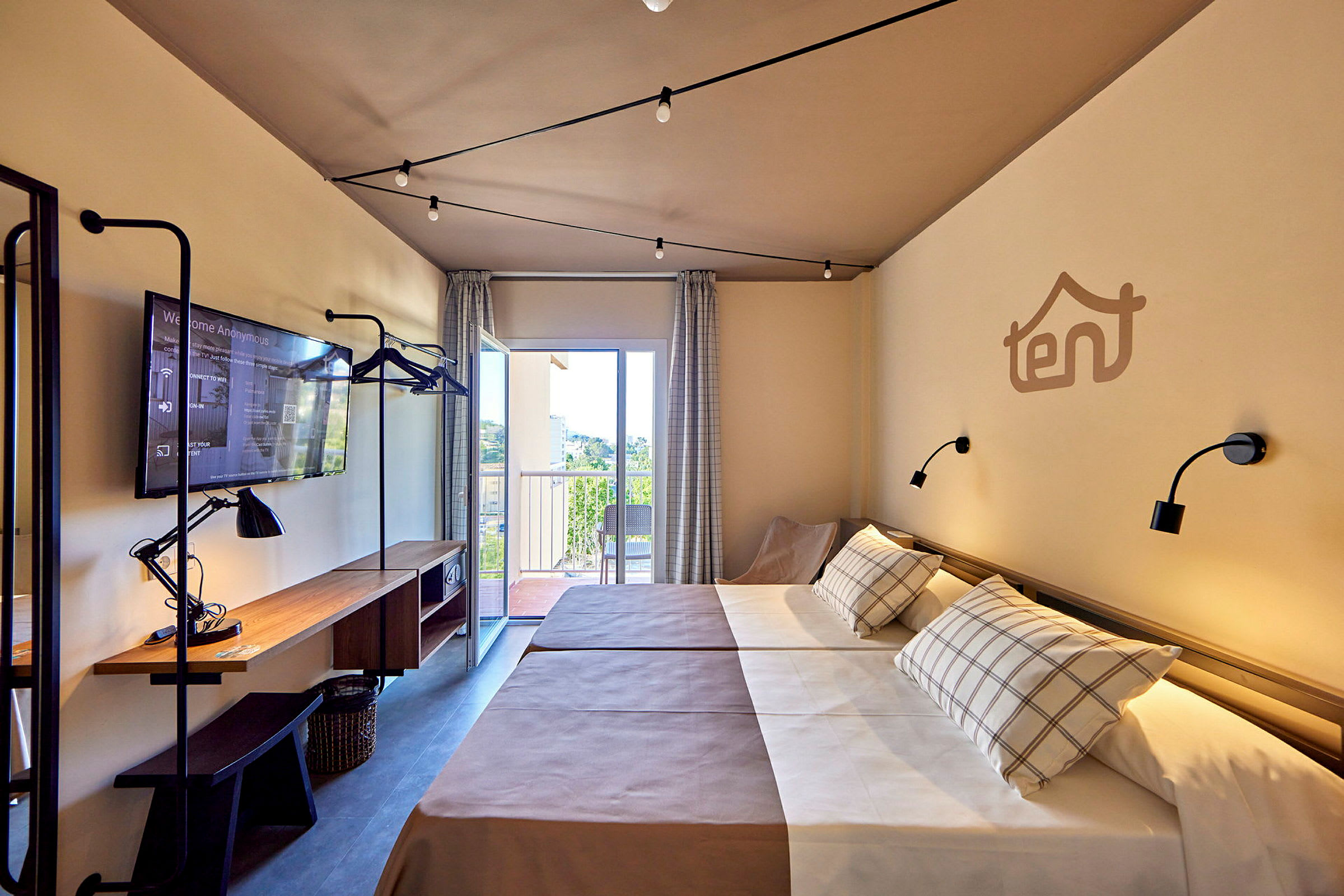 Hotellrum med två enkelsängar, arbetsbord med lampa och TV, samt balkong med utsikt. (AI-genererad text)